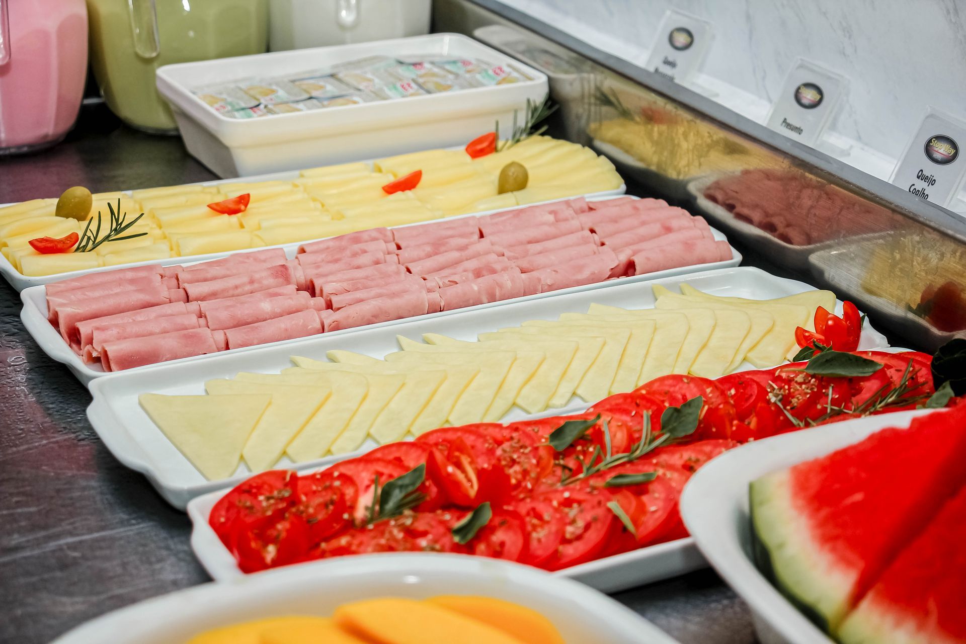 Buffet de café da manhã com presunto, queijo, tomate e fatias de melancia.