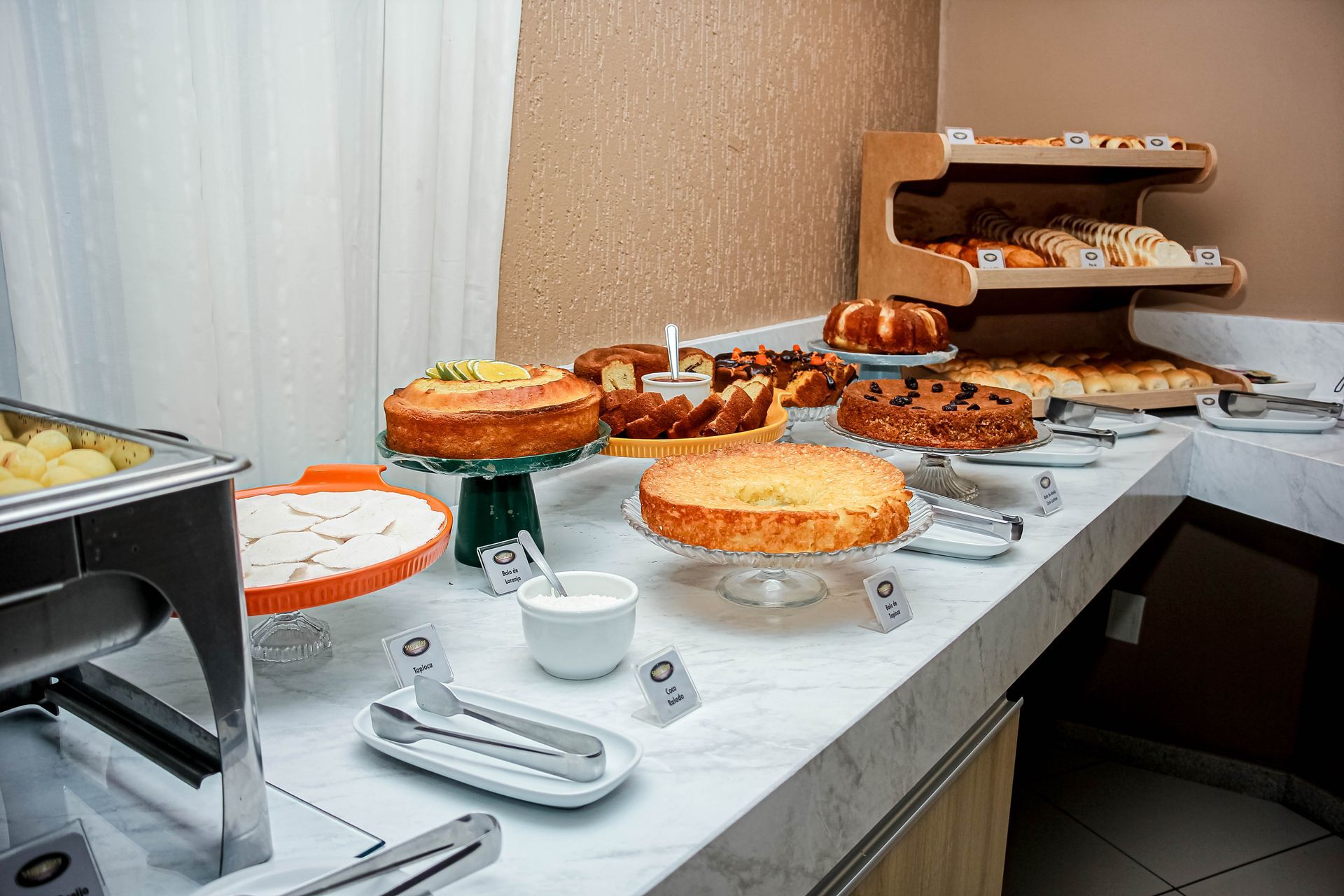 Buffet com bolos e doces em bancada de mármore. Um ambiente aconchegante para o café da manhã.