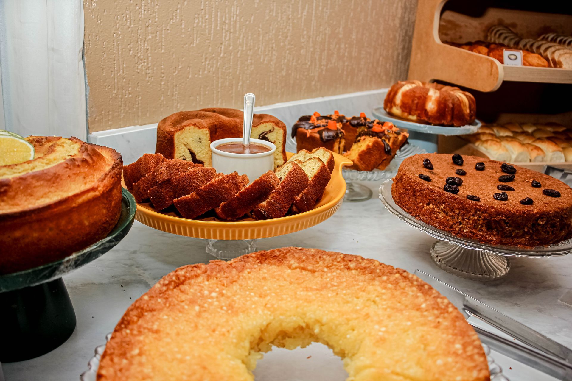 Bolos em exposição: vários bolos bundt e redondos em suportes, com uma tigela de molho para mergulhar.