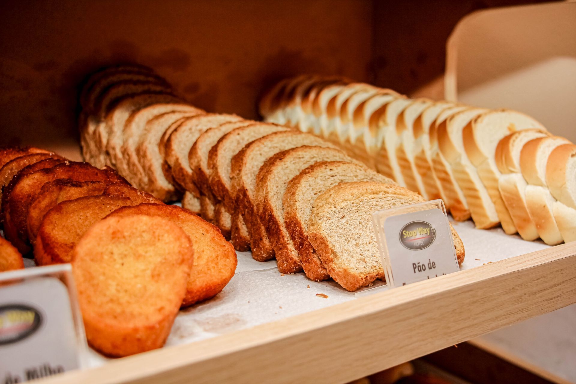 As prateleiras exibem muffins e pães fatiados: integral e branco. Disposição em madeira.
