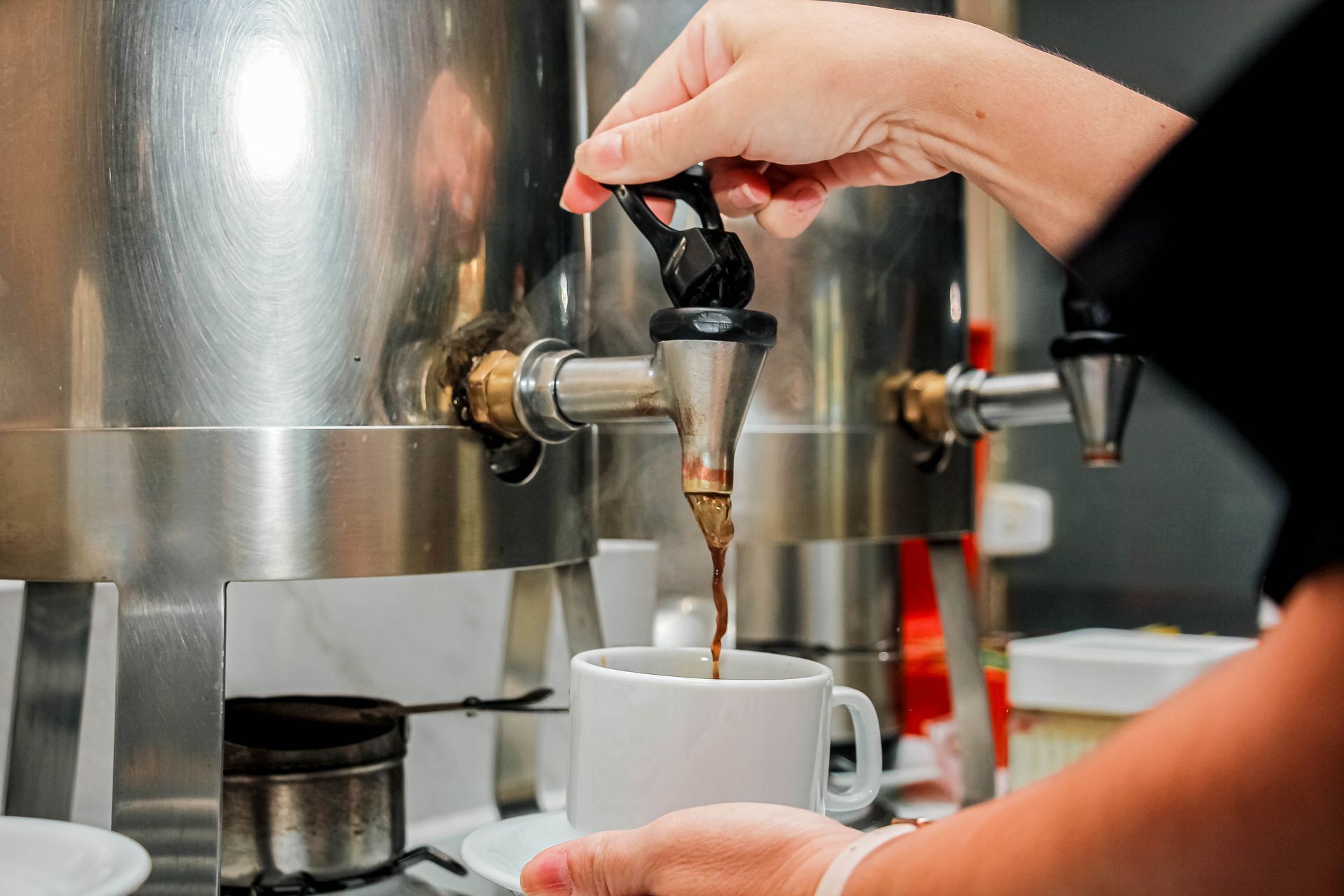 Uma pessoa despeja café de um dispensador em uma caneca branca.