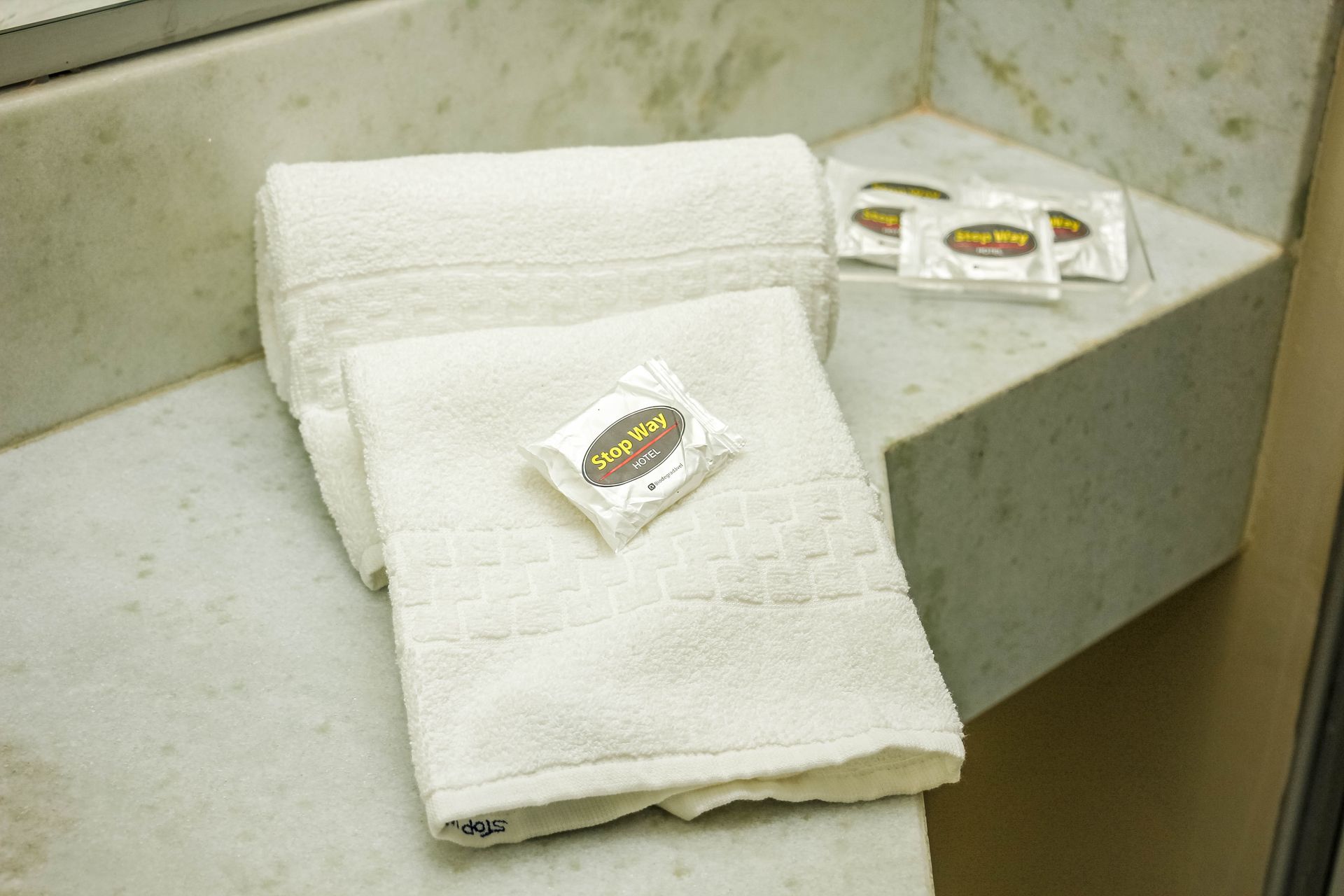 Toalhas brancas e sabonete embrulhado em uma prateleira de mármore em um banheiro.