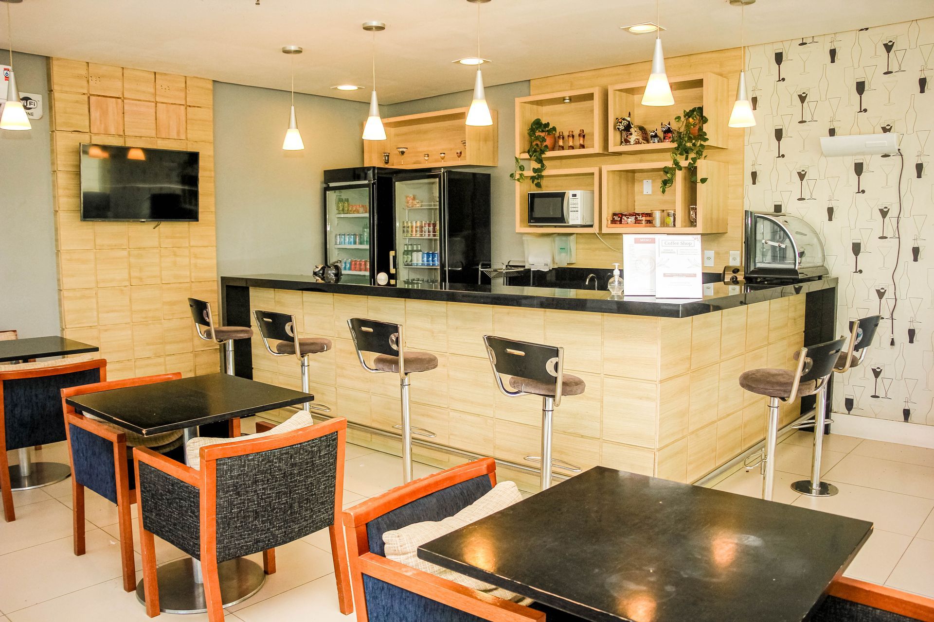 Bar com bancos, mesas com cadeiras. Geladeiras, armários e um micro-ondas são visíveis.