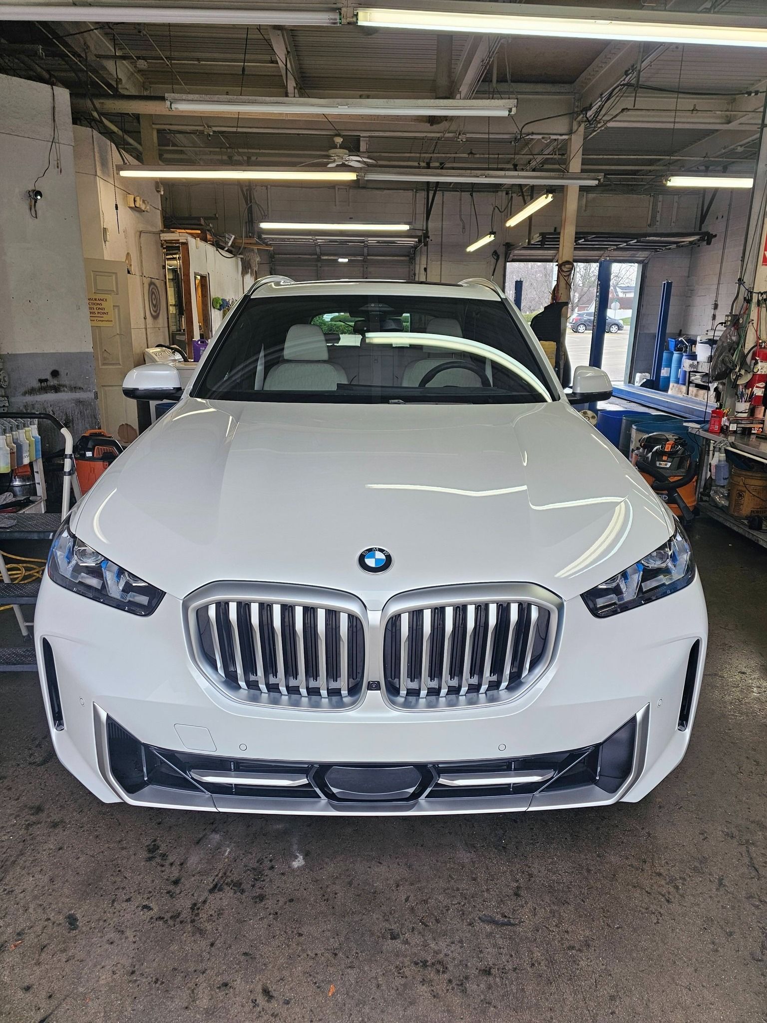 A person wearing gloves uses a paint spray gun to coat a dark car panel in a workshop.
