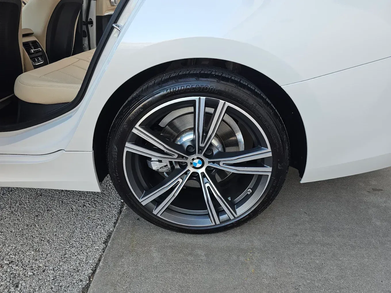 A person wearing black gloves uses a small brush to clean the textured steering wheel of a car interior.