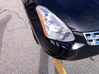Close-up of the front passenger-side headlight and bumper of a black sedan parked on asphalt near a painted yellow line.