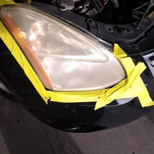 A car headlight taped off with yellow masking tape in preparation for restoration.
