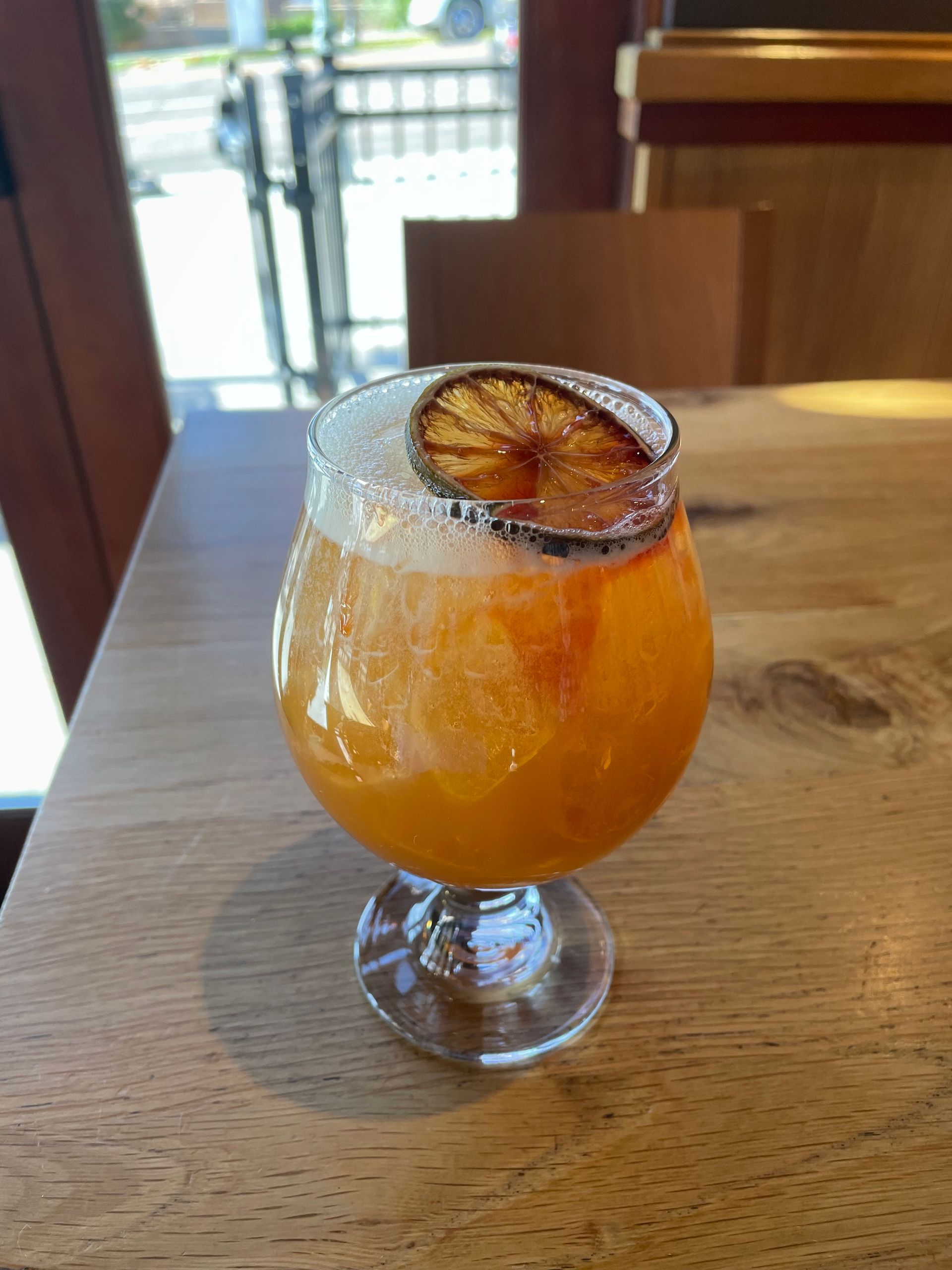 Orange cocktail in a stemmed glass, garnished with a dehydrated orange slice on a wooden table.