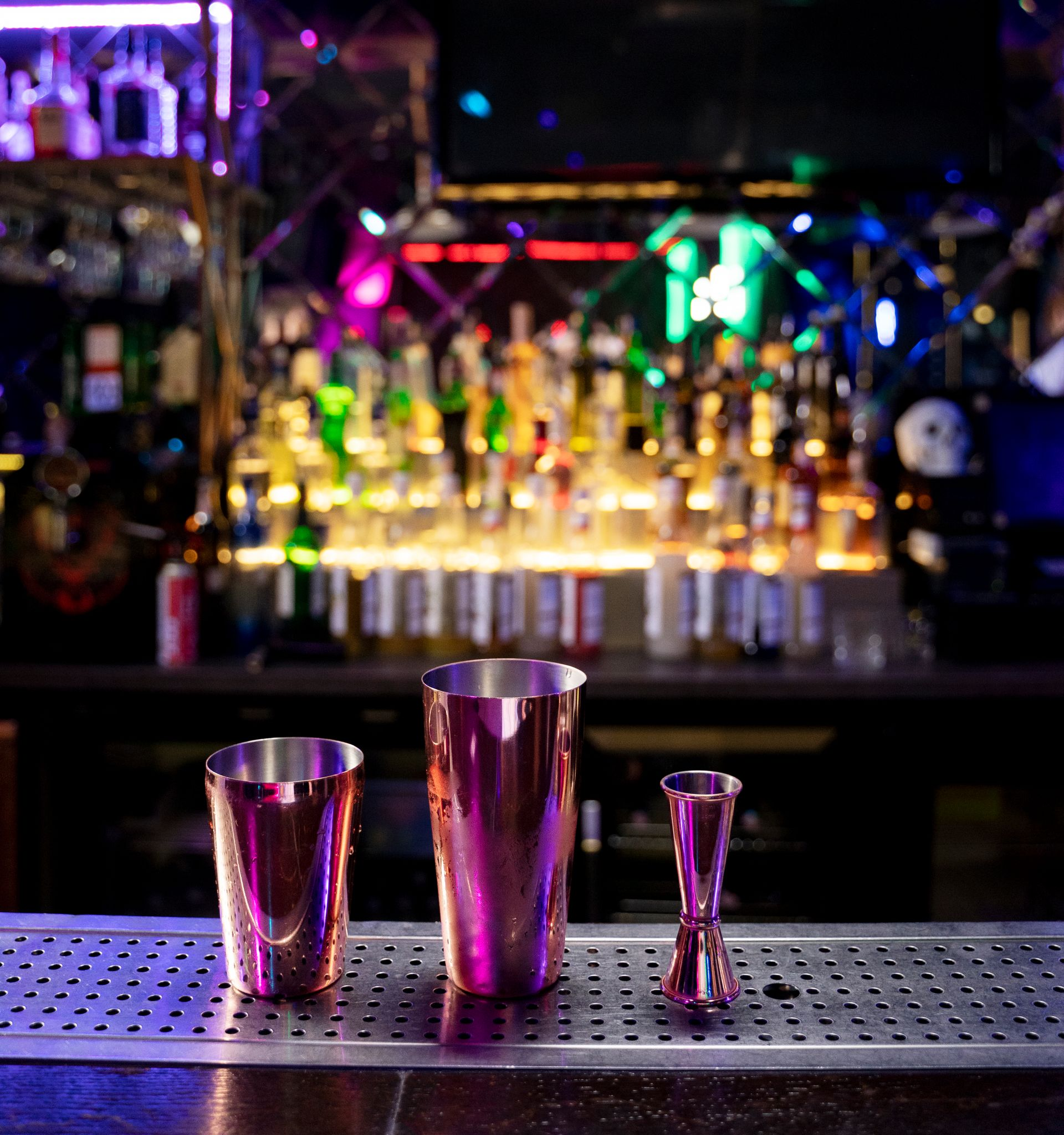 Cocktail shaker set on a bar, with bottles and neon lights in the background.
