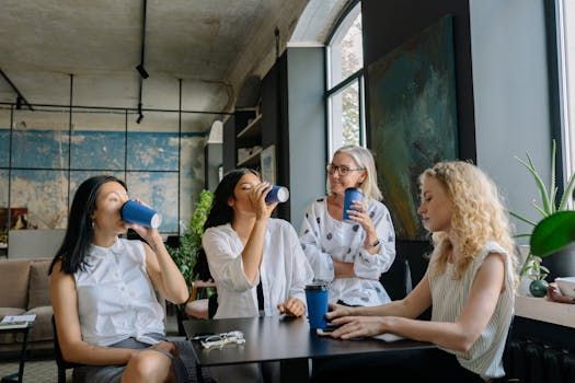 Four people chatting and drinking coffee at a cafe table by a window