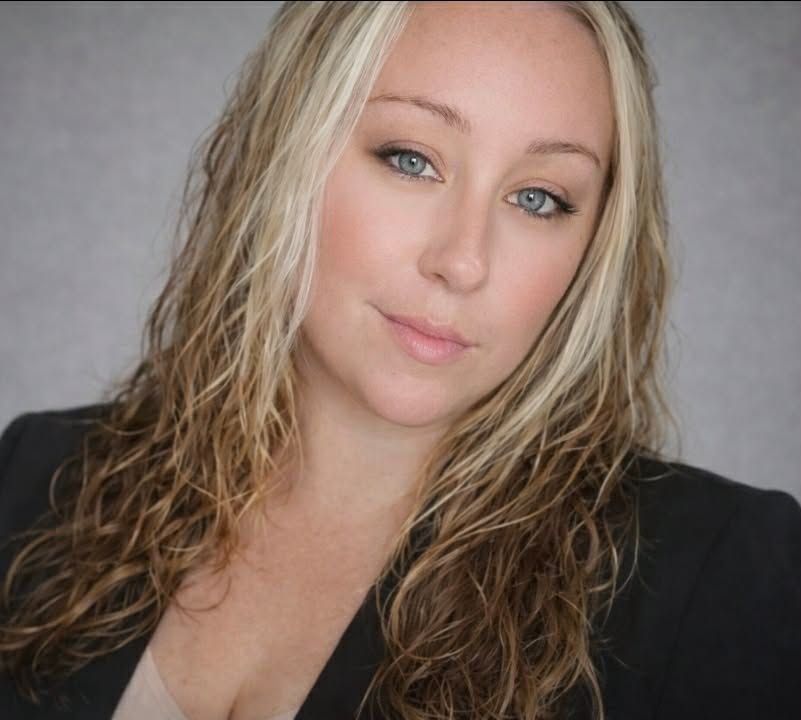 Woman with blonde hair, wearing a dark blazer, looking at the camera with a slight smile.