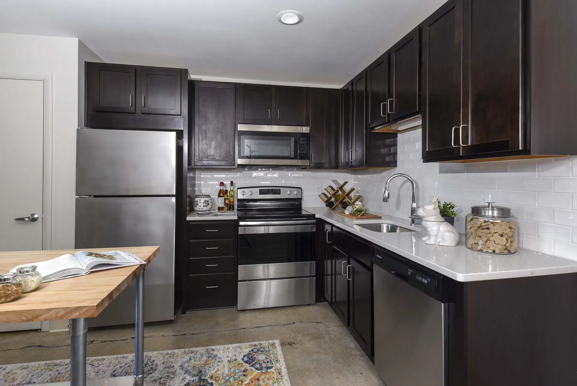 Modern kitchen with dark wood cabinets, stainless steel fridge and range, white subway tile backsplash, and a wooden prep table at Terminal 21, a premier apartment community in Downtown Pittsburgh, Pennsylvania.