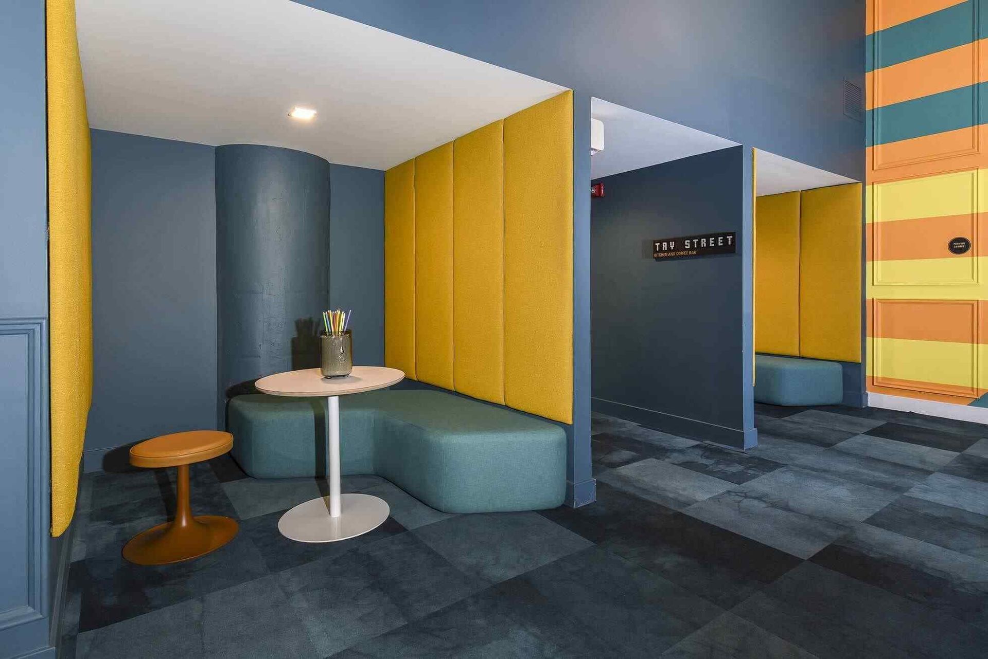 Colorful residential lounge with blue walls, yellow padded dividers, and a round table at Terminal 21, a premier apartment community in Downtown Pittsburgh, Pennsylvania.