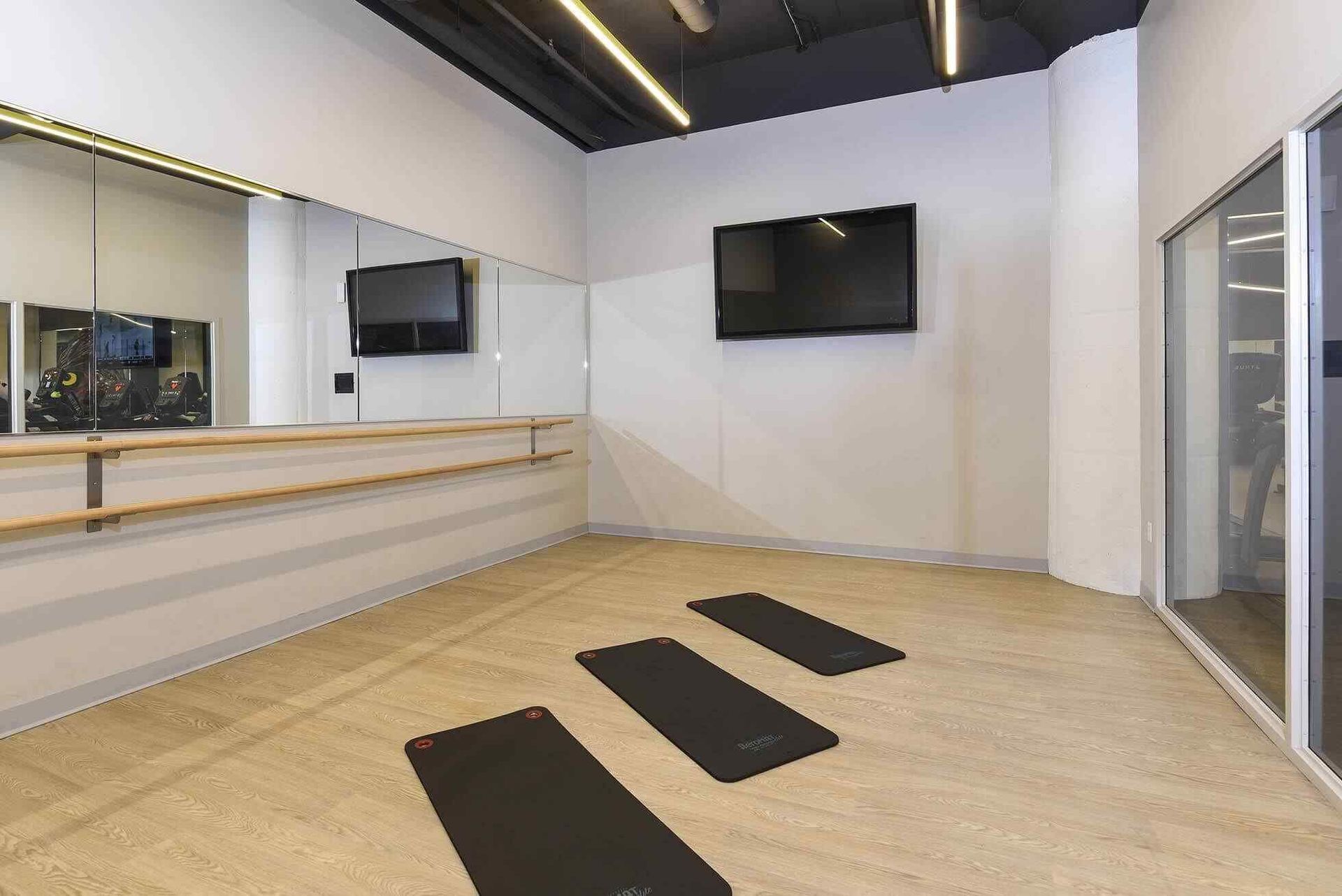 Fitness room with mirrors, three yoga mats on a wood floor, and a wall-mounted TV at Terminal 21, a premier apartment community in Downtown Pittsburgh, Pennsylvania.