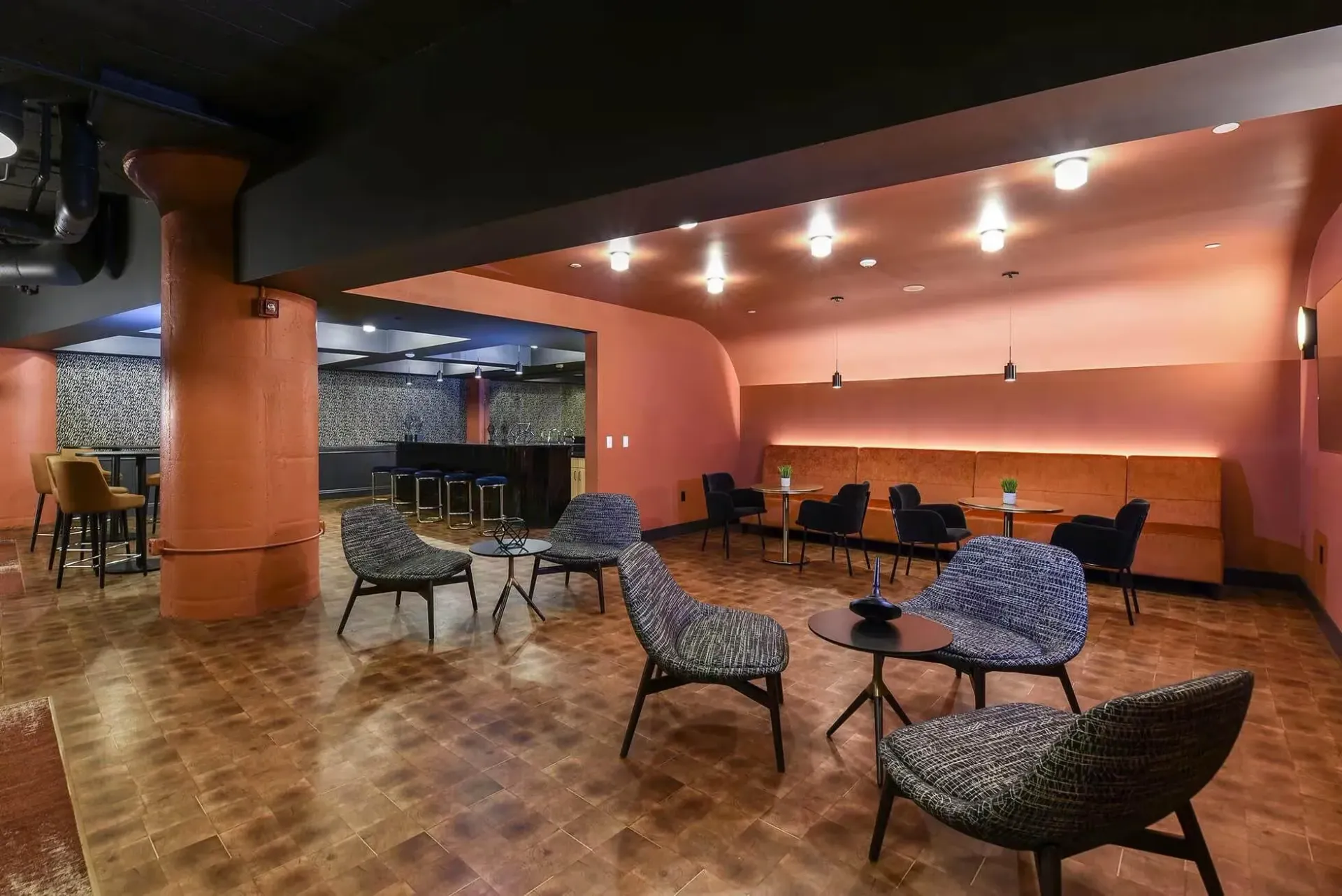 Interior community lounge with curved pink walls, lounge chairs, and a bar area at Terminal 21, a premier apartment community in Downtown Pittsburgh, Pennsylvania.
