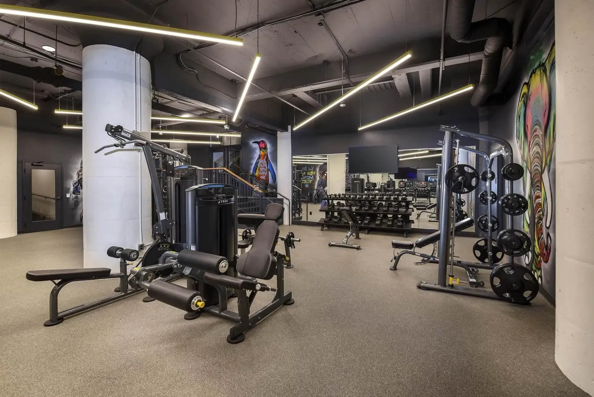 Industrial-style fitness center with weight machines, benches, free weights, and mirrors at Terminal 21, a premier apartment community in Downtown Pittsburgh, Pennsylvania.
