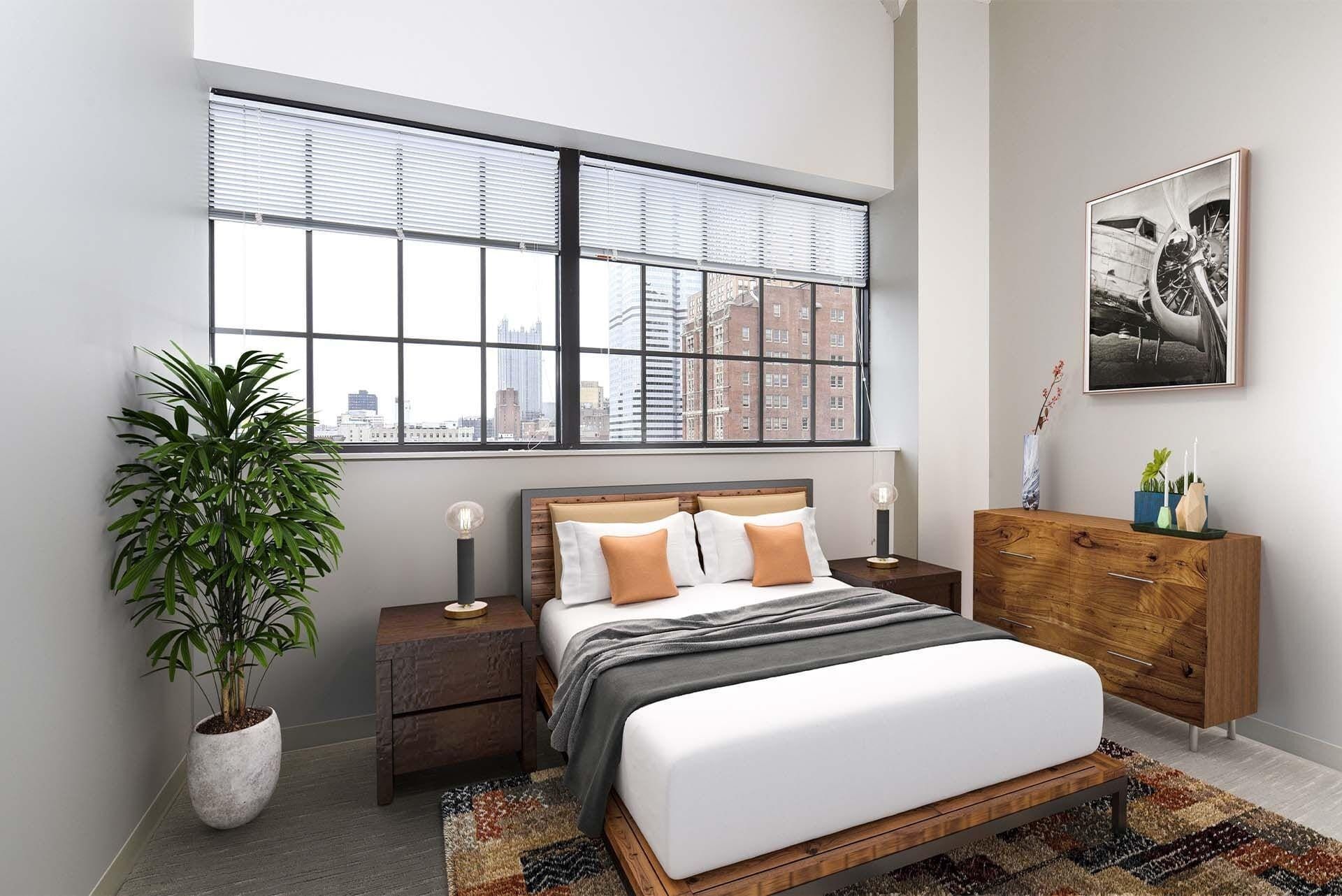 Bedroom with a large window, blinds, a potted plant, and wooden bed frame with nightstands at Terminal 21, a premier apartment community in Downtown Pittsburgh, Pennsylvania.