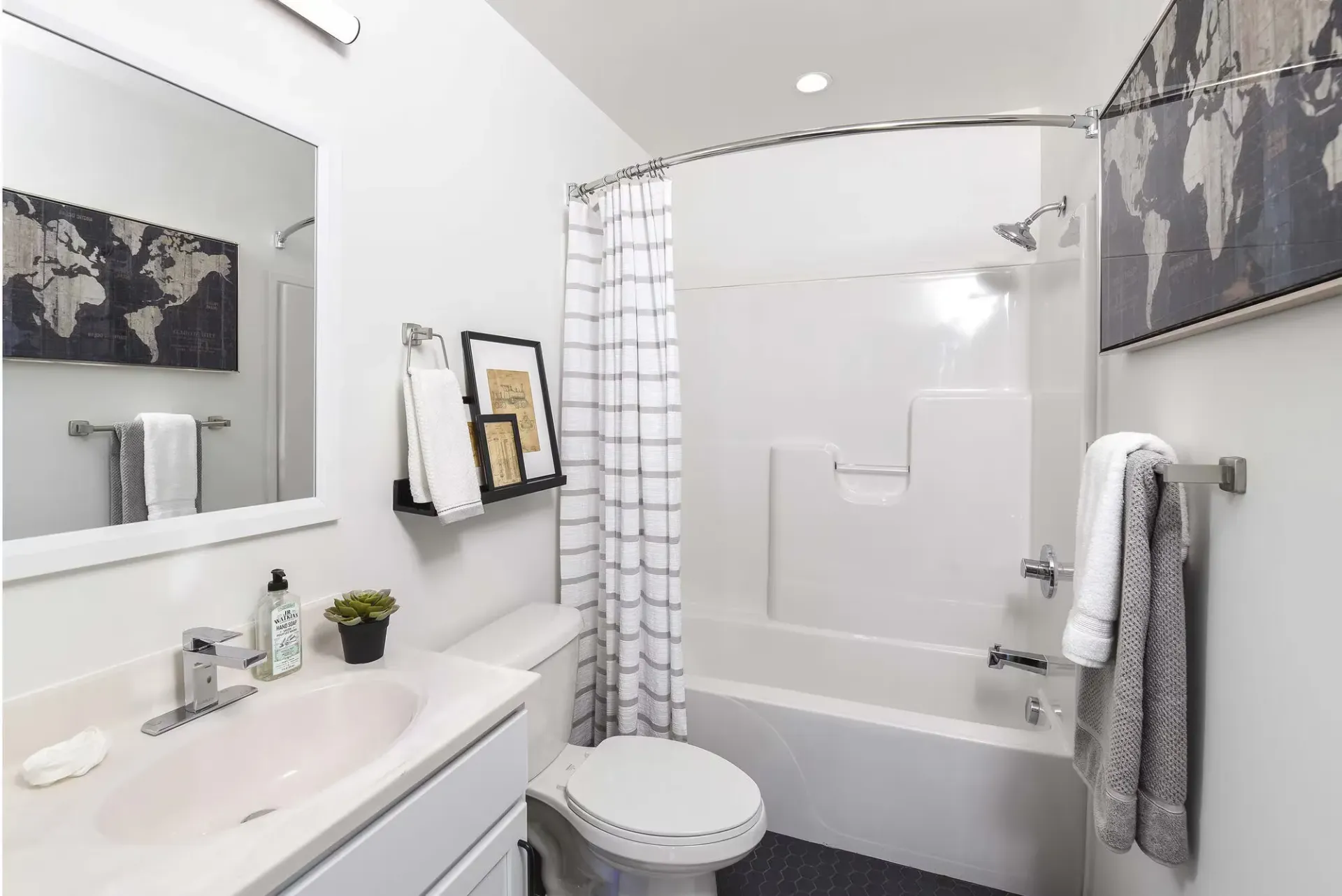 Bright apartment bathroom with vanity, mirror, toilet, and curved shower/tub with striped curtain at Terminal 21, a premier apartment community in Downtown Pittsburgh, Pennsylvania.