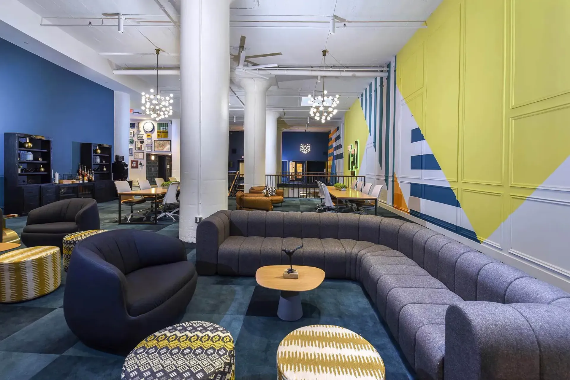 Colorful modern community lounge with curved gray sectional, round ottomans, and bright mural at Terminal 21, a premier apartment community in Downtown Pittsburgh, Pennsylvania.