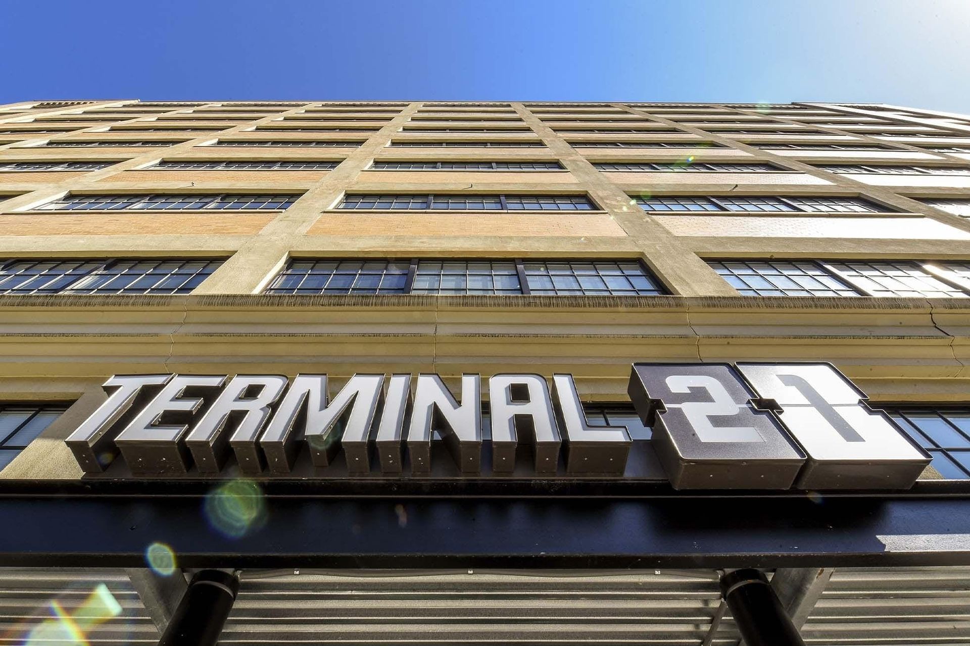 Low-angle view of a tall brick apartment building with a large Terminal 21 sign at the base.