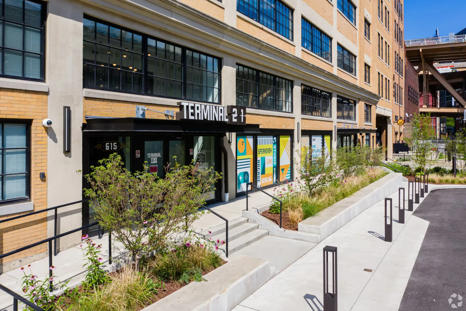 Exterior view of a brick apartment building with a storefront labeled Terminal 21 and a landscaped walkway.
