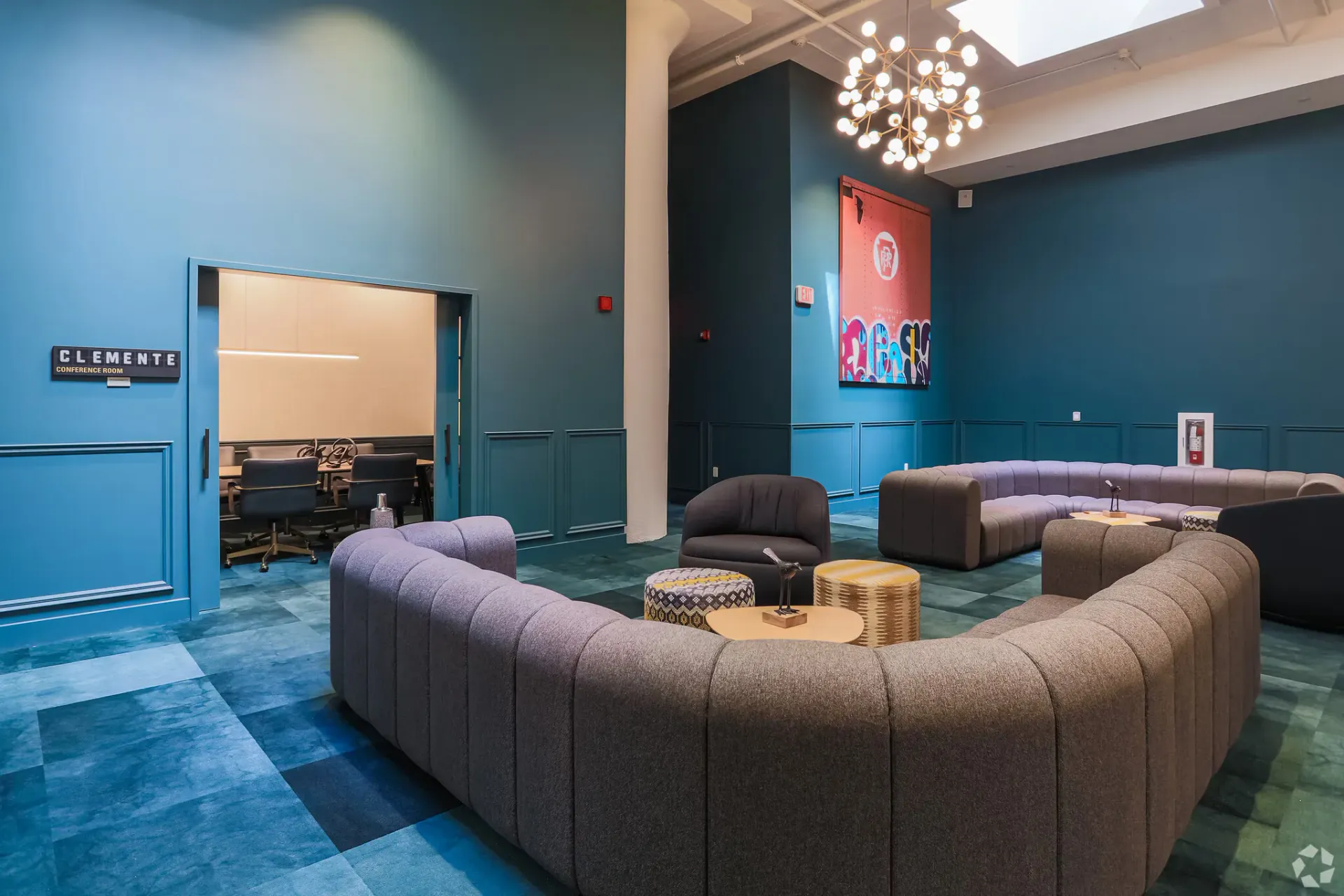 Teal-walled lounge with curved gray sectional seating and a conference room doorway at Terminal 21, a premier apartment community in Downtown Pittsburgh, Pennsylvania.