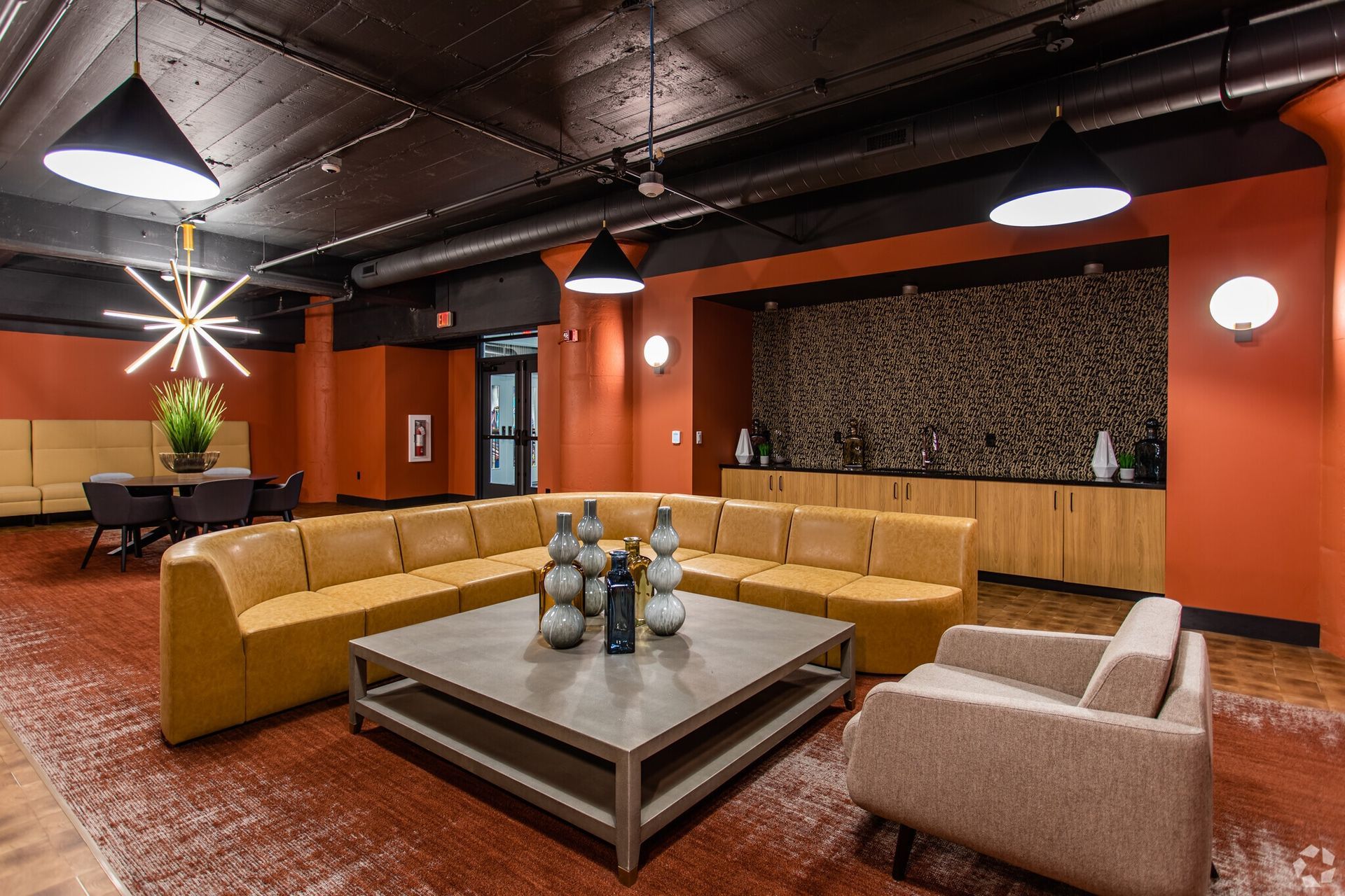 Indoor community lounge with orange walls, tan sectional seating, and a modern coffee table at Terminal 21, a premier apartment community in Downtown Pittsburgh, Pennsylvania.