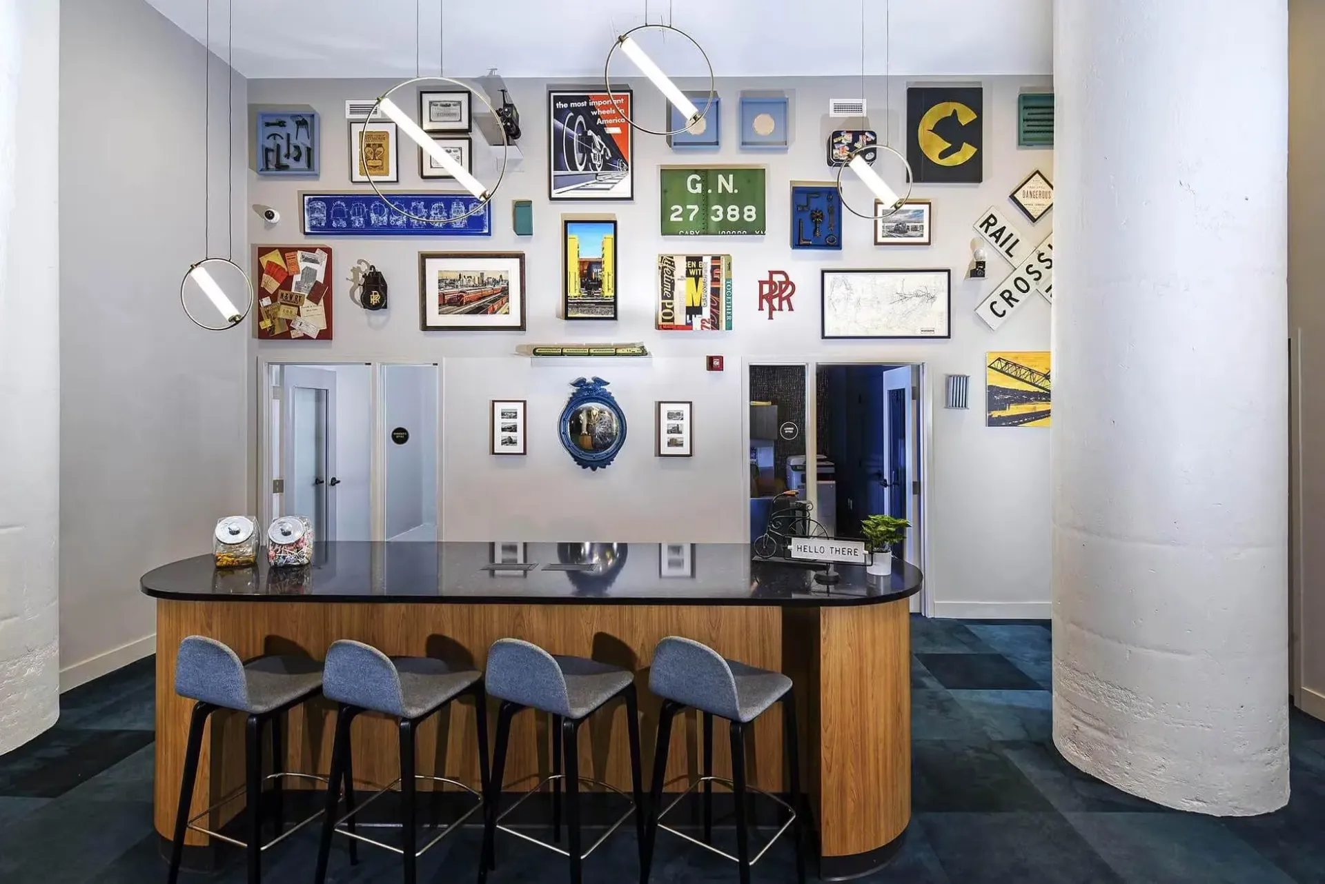 Lobby area with a curved wooden reception counter, five gray stools, and a wall filled with framed art at Terminal 21, a premier apartment community in Downtown Pittsburgh, Pennsylvania.