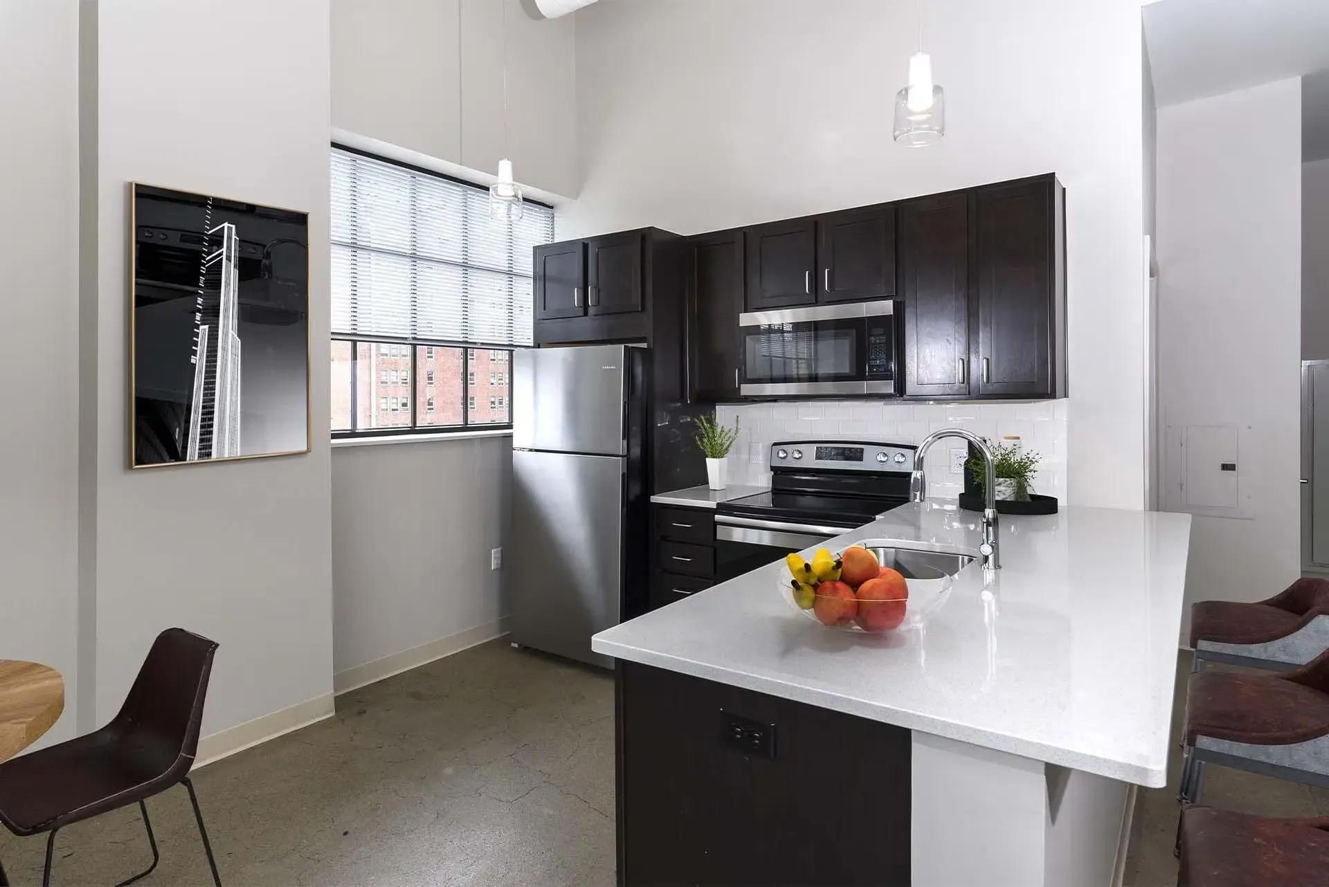 Kitchen in a modern apartment with dark wood cabinets, stainless steel appliances, and a white island at Terminal 21, a premier apartment community in Downtown Pittsburgh, Pennsylvania.