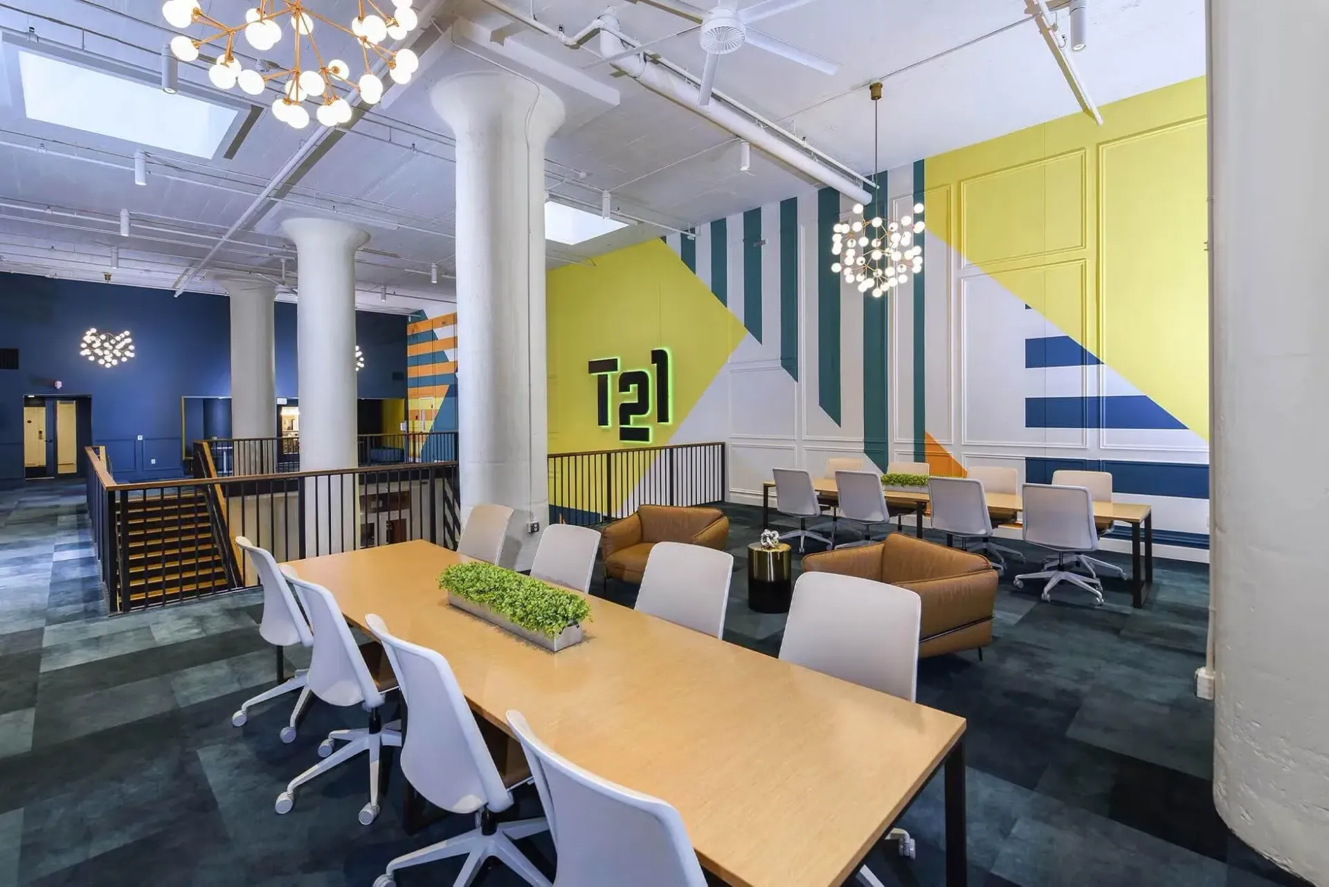Open community lounge with a long wooden table, white chairs, lounge seating, and a colorful geometric mural at Terminal 21, a premier apartment community in Downtown Pittsburgh, Pennsylvania.