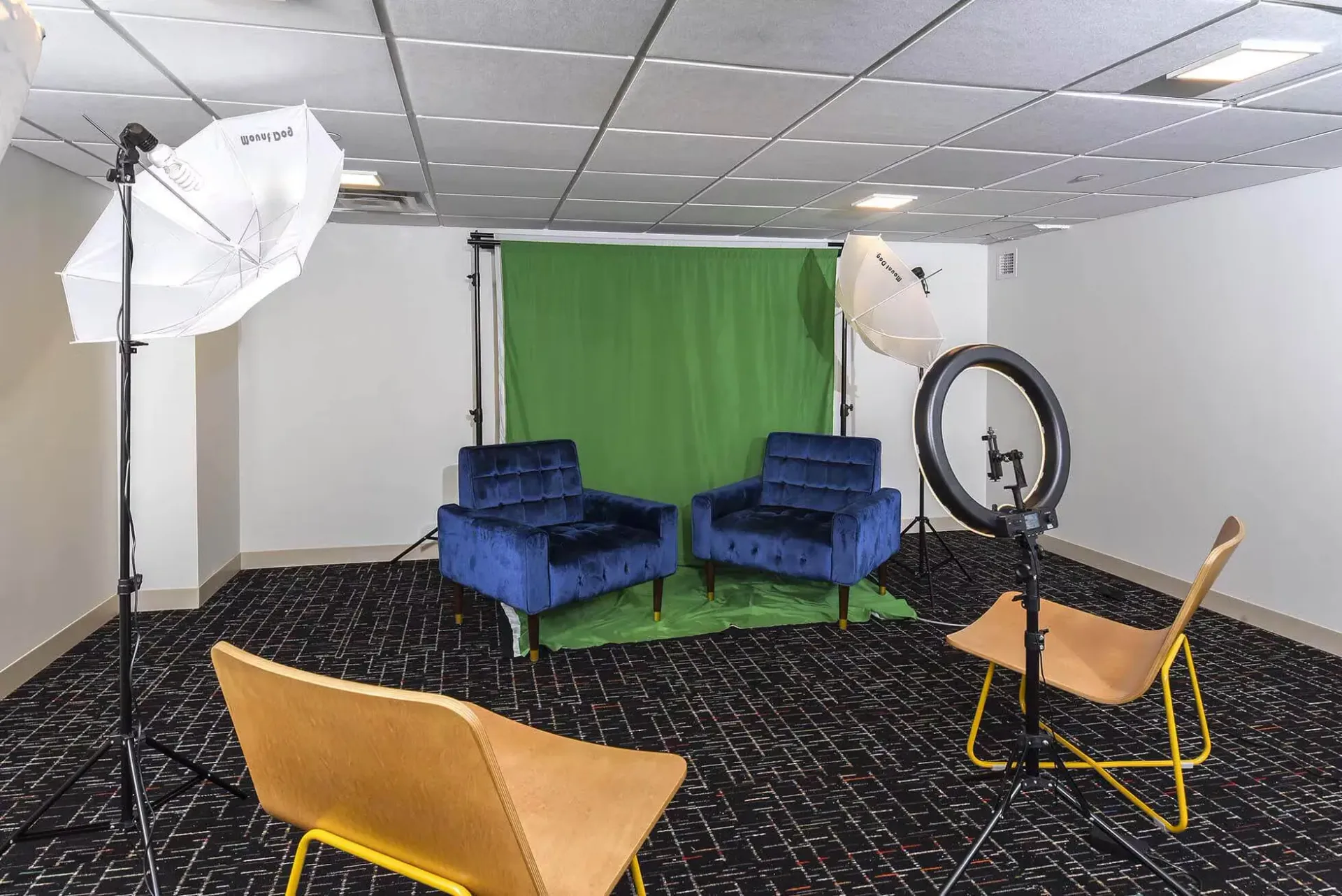 Interior photo studio with green screen backdrop, two blue chairs, and lighting equipment at Terminal 21, a premier apartment community in Downtown Pittsburgh, Pennsylvania.