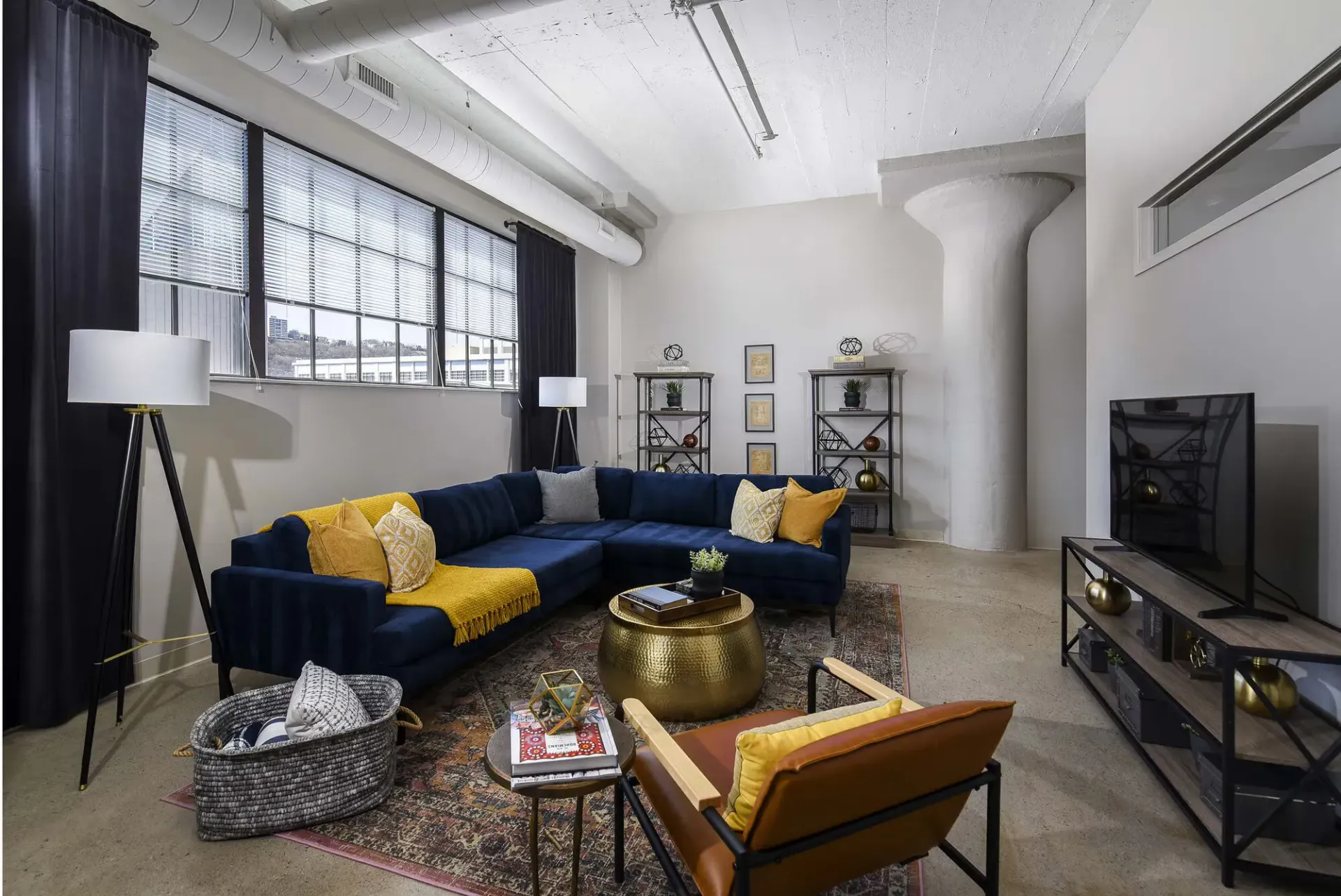 Modern apartment living room with a navy sectional, large windows, and warm gold accents at Terminal 21, a premier apartment community in Downtown Pittsburgh, Pennsylvania.