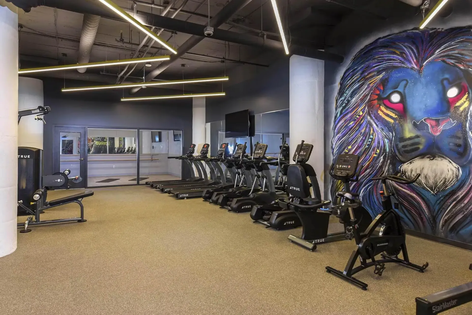 Indoor gym with treadmills and a colorful mural of a lion on the wall at Terminal 21, a premier apartment community in Downtown Pittsburgh, Pennsylvania.