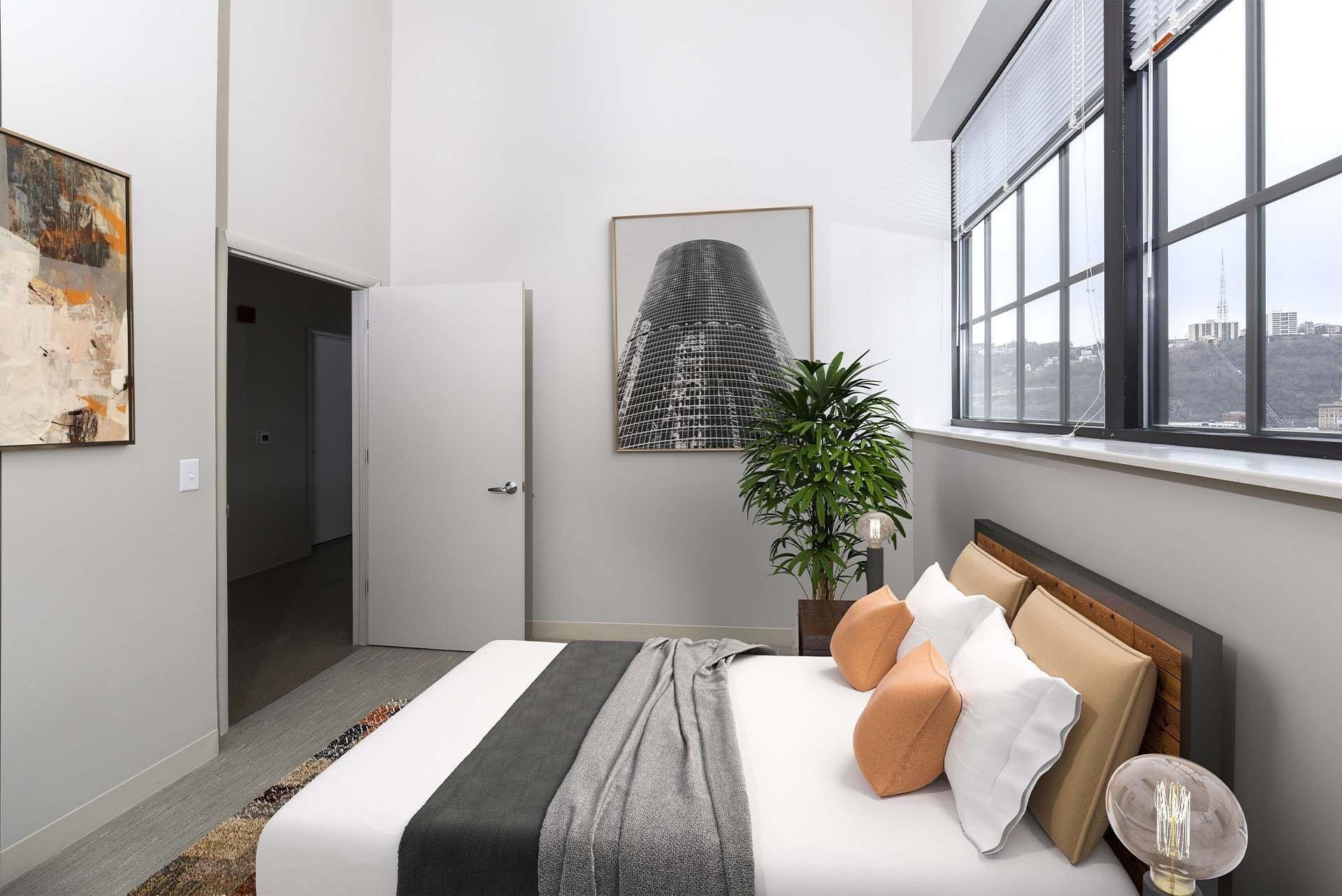 Bed in a contemporary apartment bedroom with a large grid-window, plant, and wall artat Terminal 21, a premier apartment community in Downtown Pittsburgh, Pennsylvania.