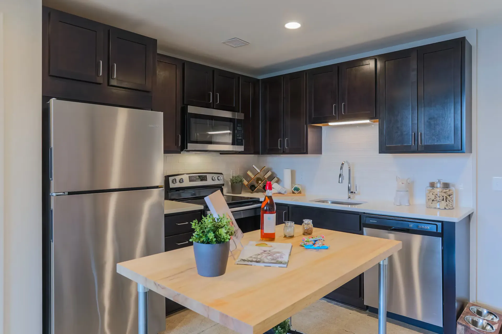 Modern kitchen in an apartment with dark wood cabinets, stainless steel appliances, and a wood island at Terminal 21, a premier apartment community in Downtown Pittsburgh, Pennsylvania.