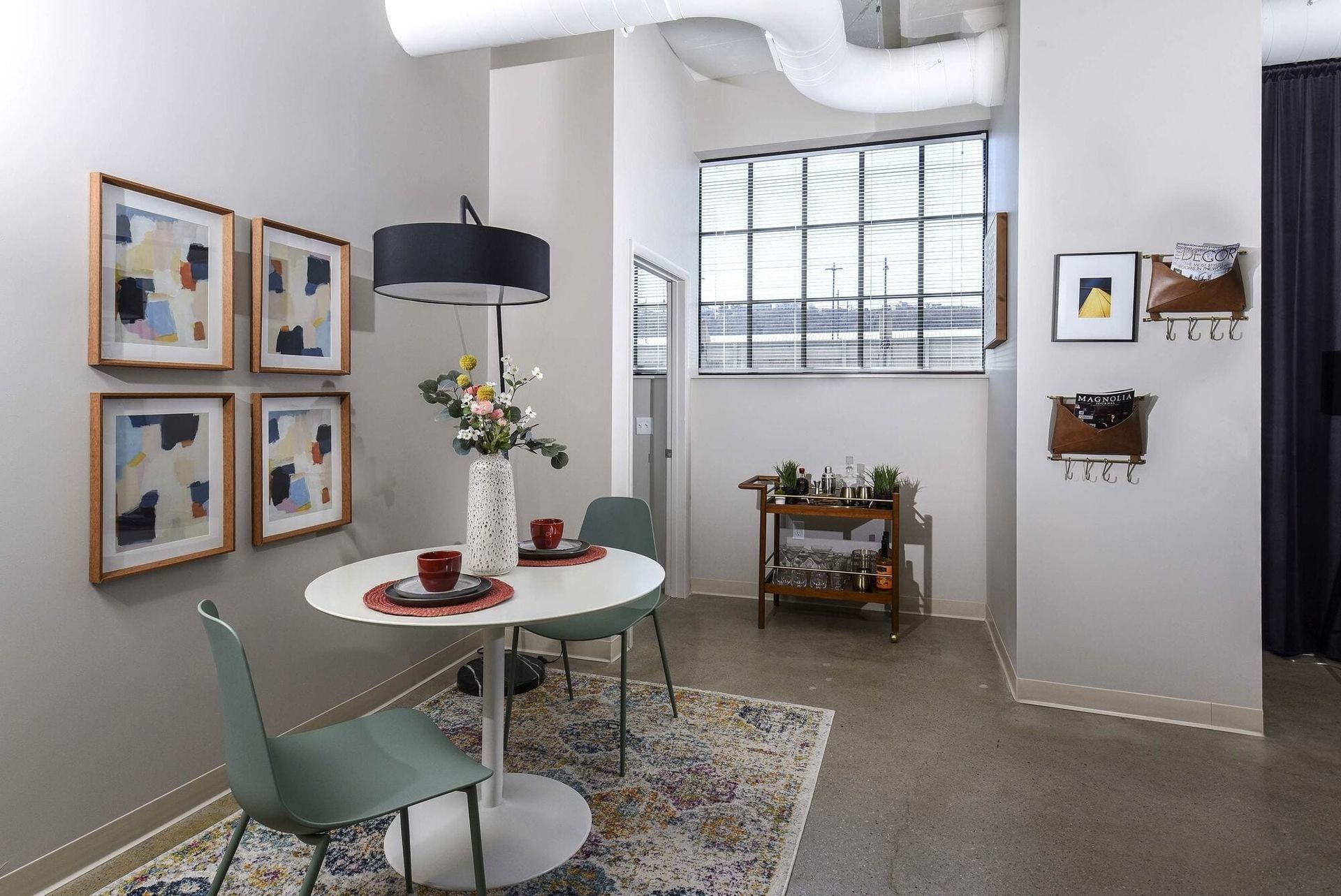 Apartment dining nook with round white table, pastel chairs, abstract art, and a bar cart by a large window at Terminal 21, a premier apartment community in Downtown Pittsburgh, Pennsylvania.