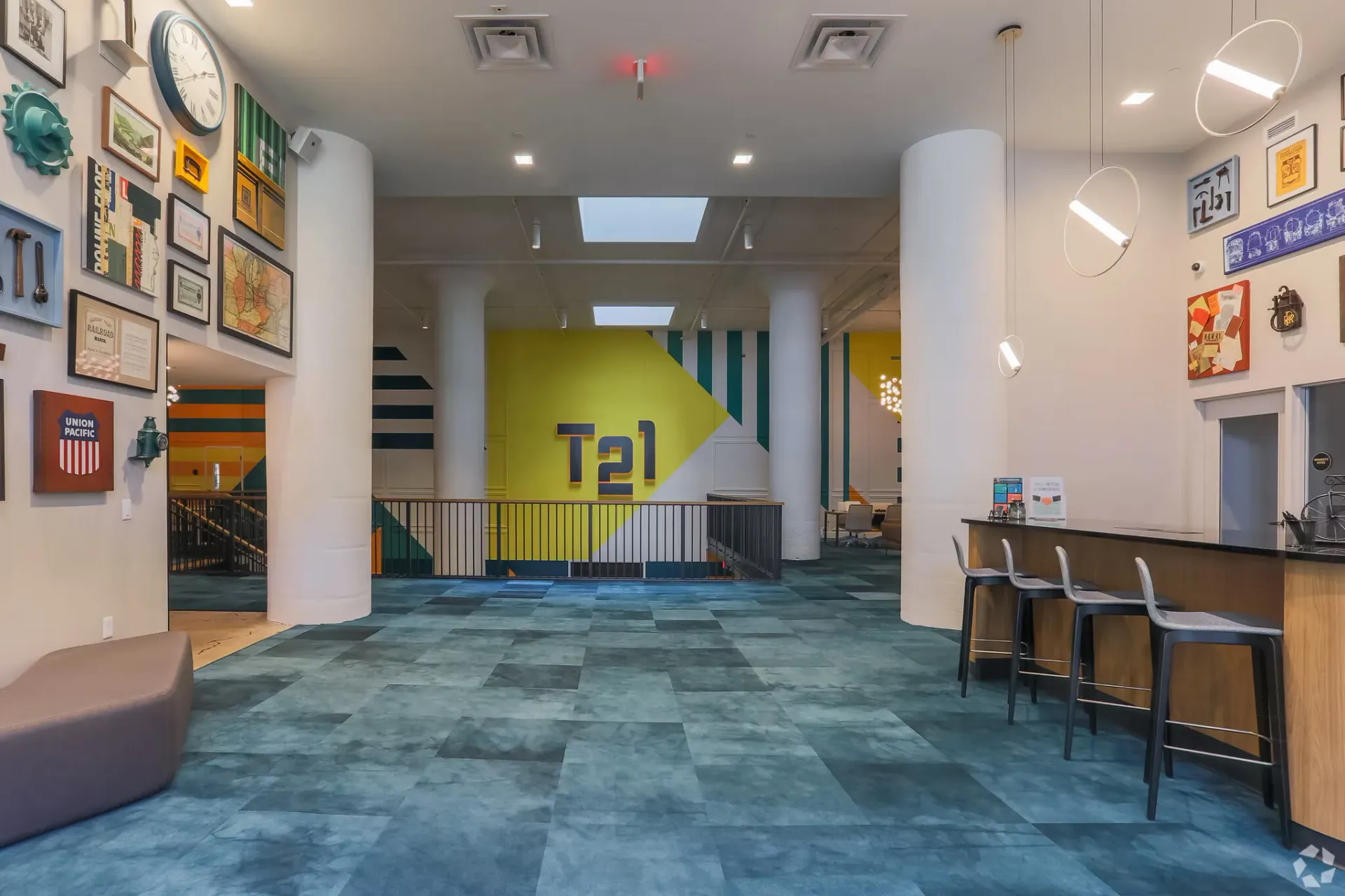 Interior community lounge with white columns, wall art, blue patterned carpet, and a bar seating area at Terminal 21, a premier apartment community in Downtown Pittsburgh, Pennsylvania.