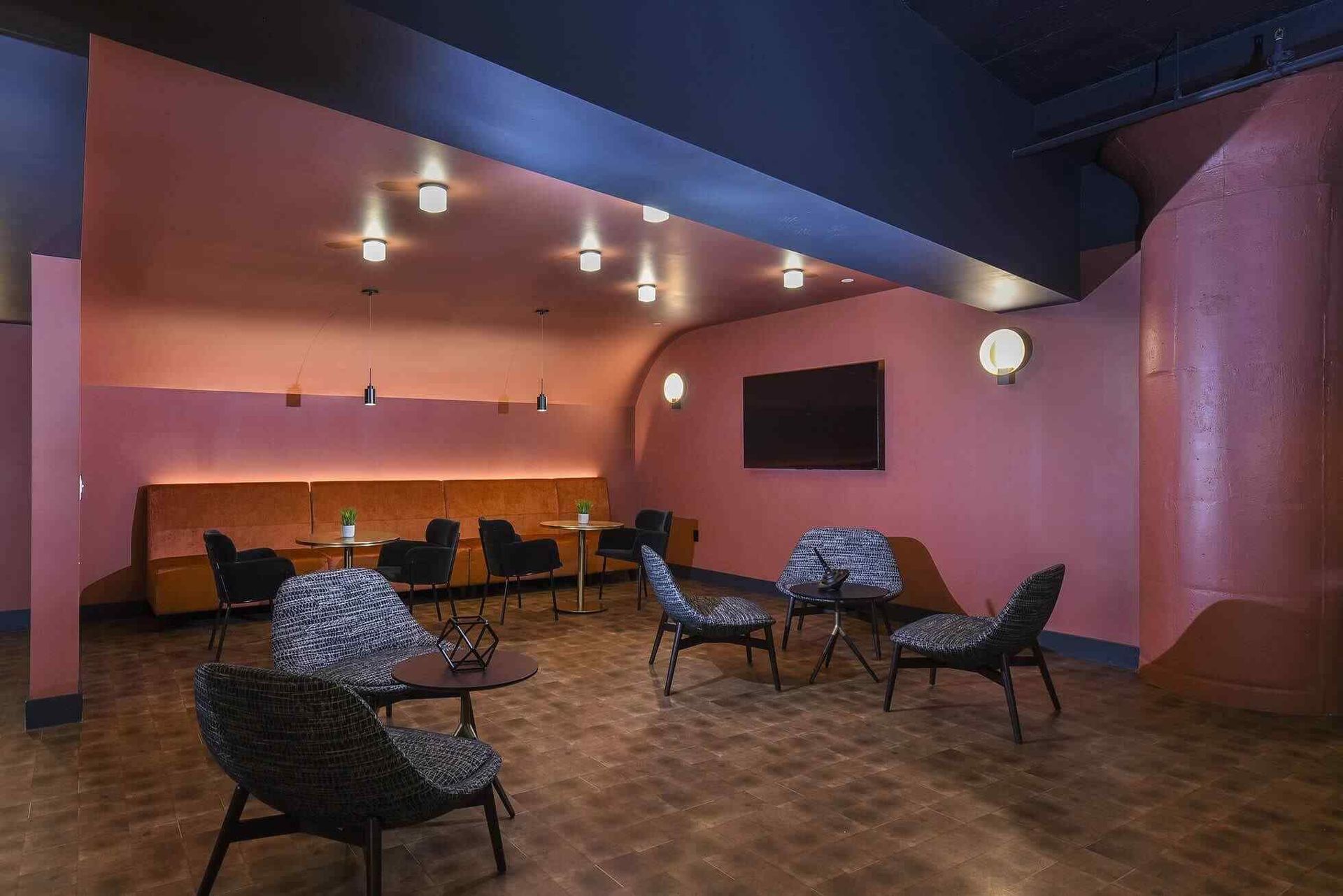 Indoor community lounge with pink walls, chairs, tables, and a wall-mounted TV at Terminal 21, a premier apartment community in Downtown Pittsburgh, Pennsylvania.