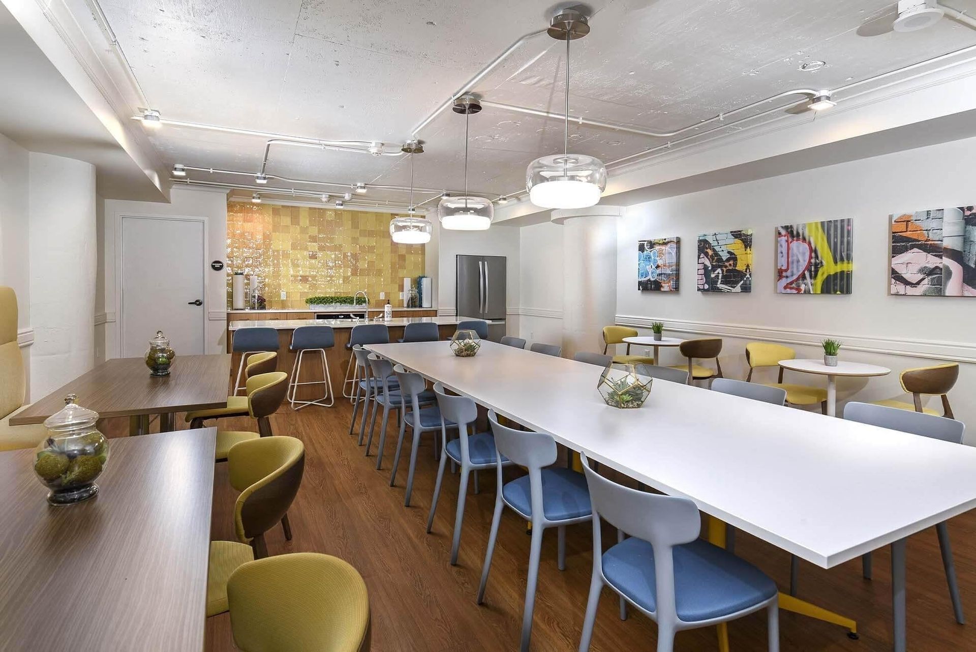 Modern community lounge with a long white table, mixed seating, and a kitchenette at Terminal 21, a premier apartment community in Downtown Pittsburgh, Pennsylvania.