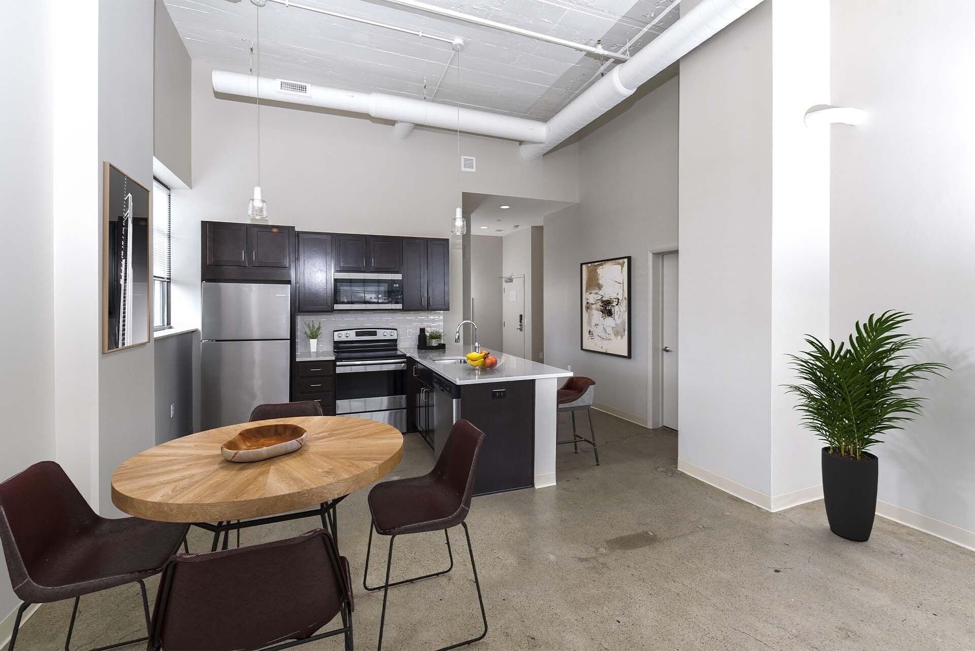 Open-concept kitchen and dining area with an island, dark cabinets, and stainless appliances at Terminal 21, a premier apartment community in Downtown Pittsburgh, Pennsylvania.