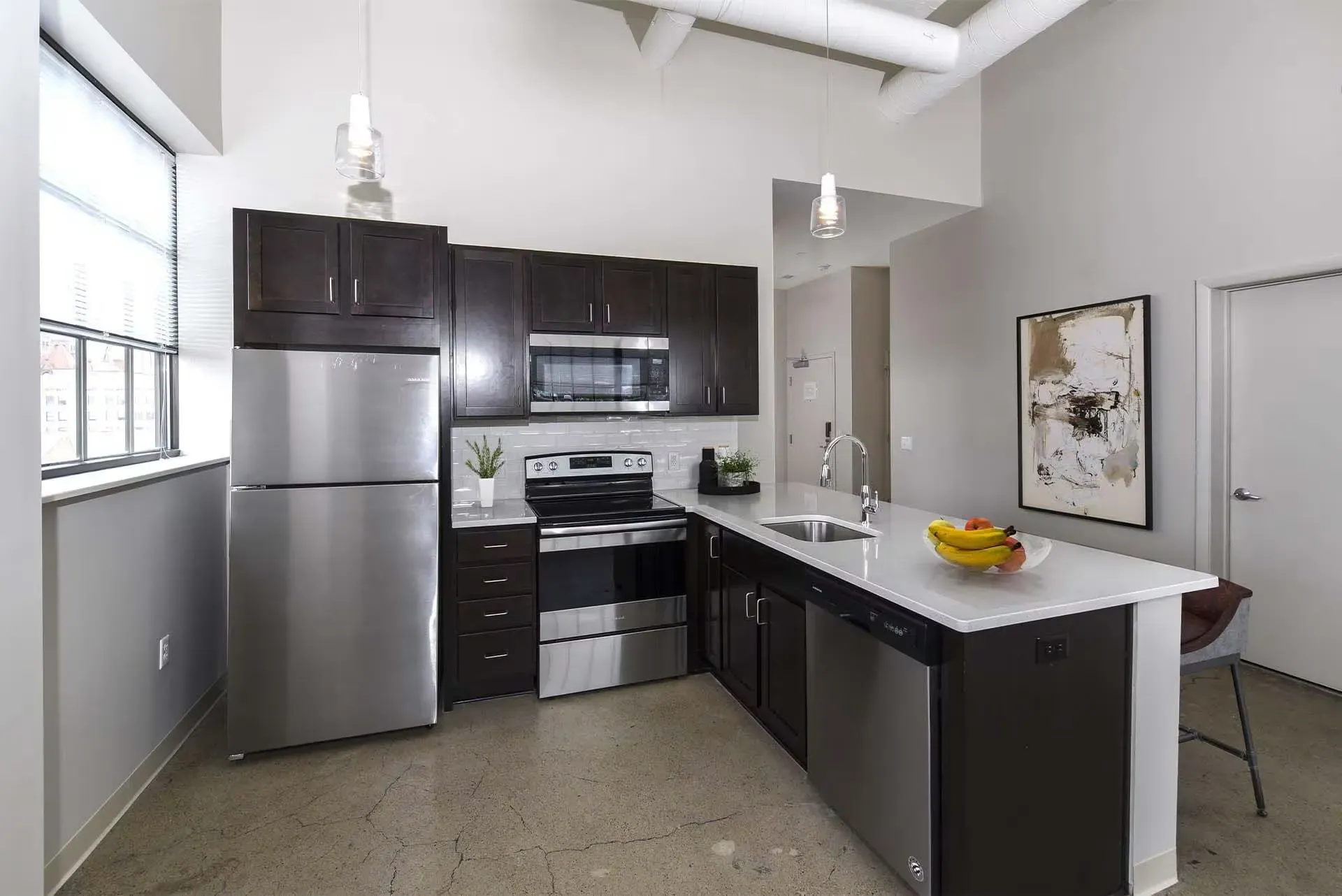 Modern apartment kitchen with stainless steel appliances, dark wood cabinets, and a large island at Terminal 21, a premier apartment community in Downtown Pittsburgh, Pennsylvania.