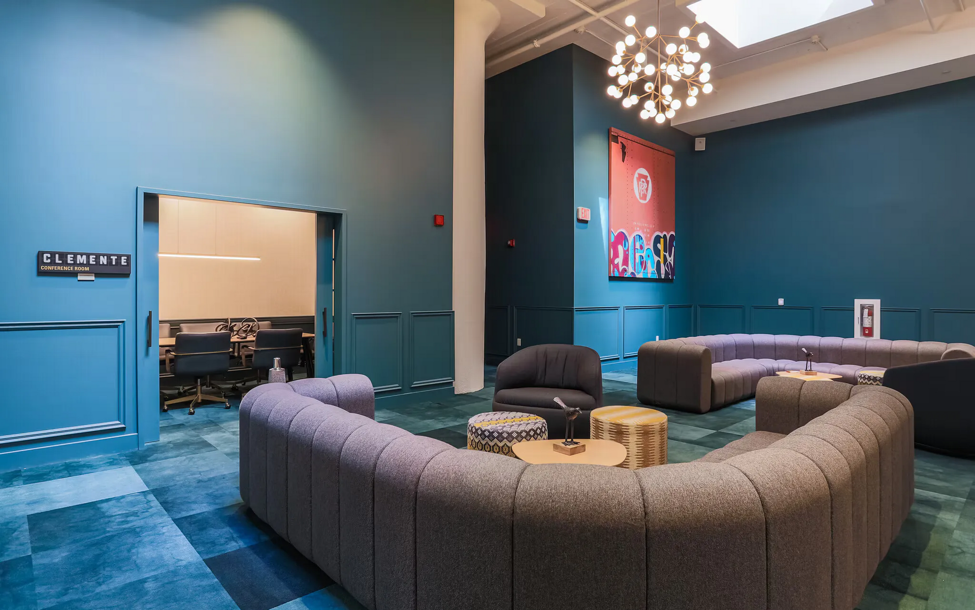 Teal-walled lounge with curved gray sectional seating and a conference room doorway at Terminal 21, a premier apartment community in Downtown Pittsburgh, Pennsylvania.