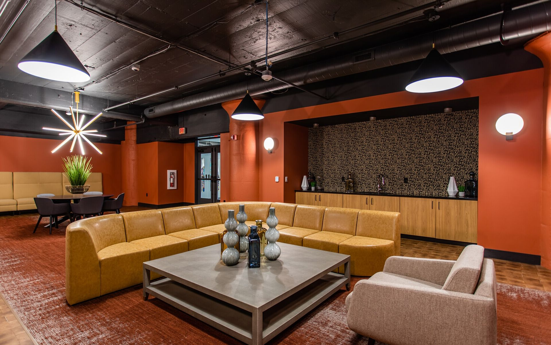 Indoor community lounge with orange walls, tan sectional seating, and a modern coffee table at Terminal 21, a premier apartment community in Downtown Pittsburgh, Pennsylvania.