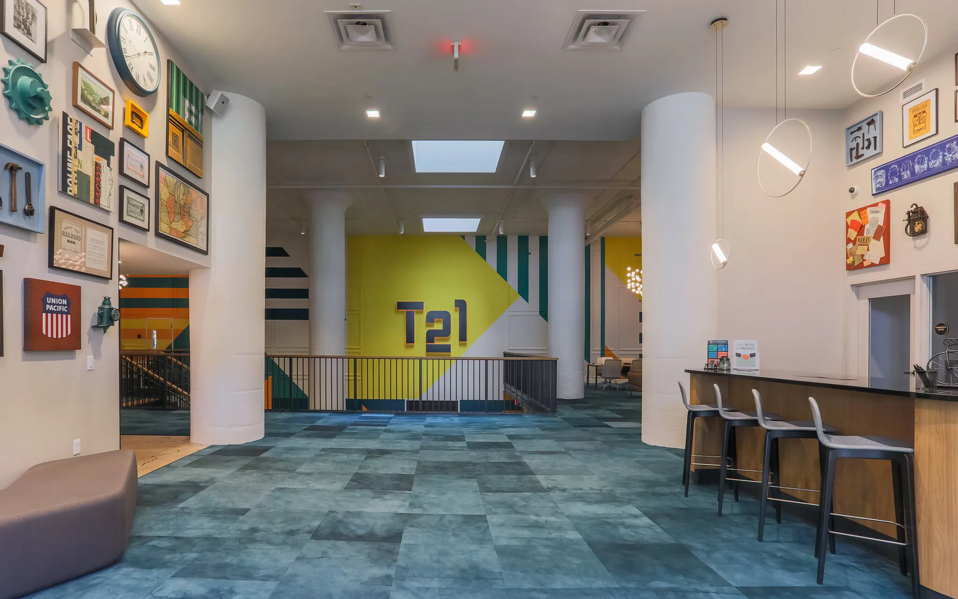 Interior community lounge with white columns, wall art, blue patterned carpet, and a bar seating area at Terminal 21, a premier apartment community in Downtown Pittsburgh, Pennsylvania.