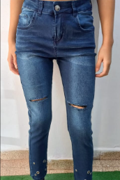 Vaqueros pitillo de mezclilla azul con rodillas rotas y adornos plateados en los tobillos.