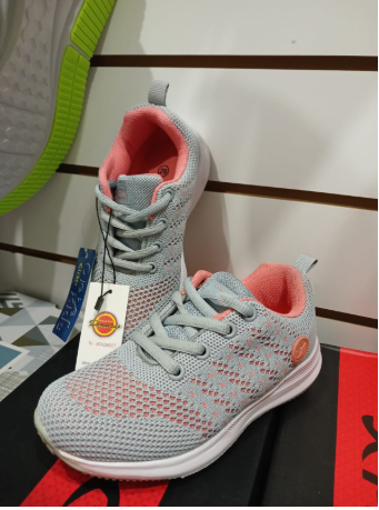 Zapatillas grises y rosas con suela blanca y etiqueta colgante en una caja negra.