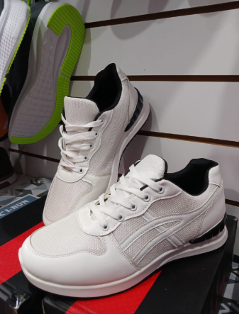 Zapatillas blancas con detalles en negro exhibidas en un estante, con otro par visible en el fondo.