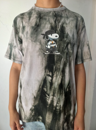 Persona con una camiseta tie-dye del personaje de Snoop Dogg. Colores gris oscuro y negro.