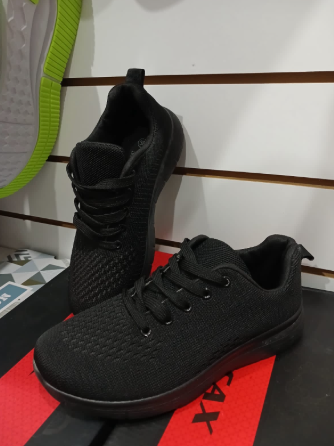 Zapatillas negras en una caja roja. Se ve otro zapato con suela verde.