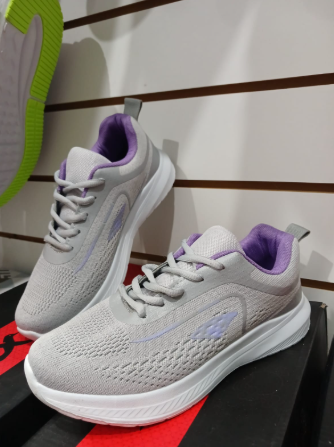 Zapatillas deportivas en exposición de color gris y morado, con suela y cordones de color blanco.